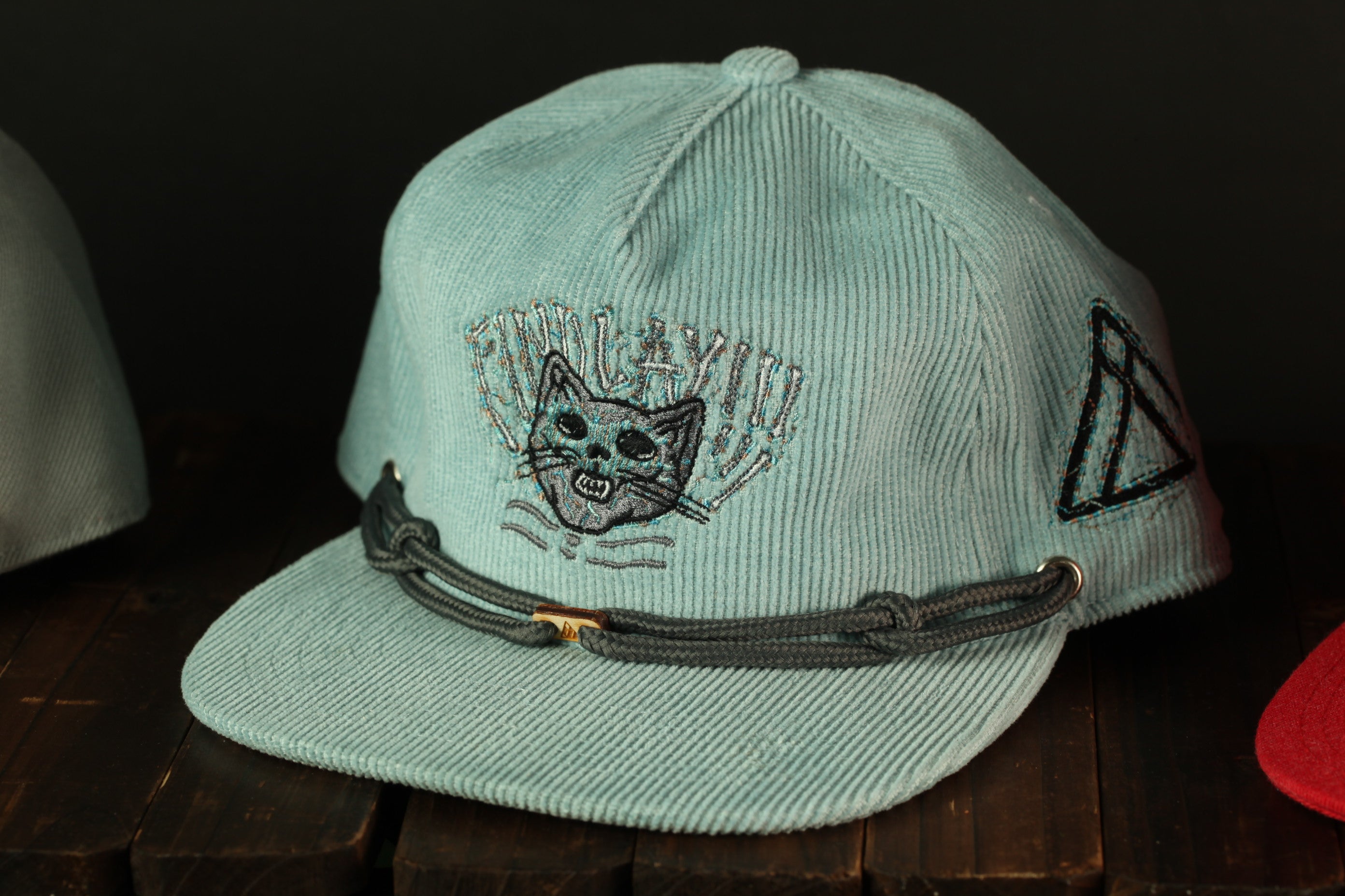 A light blue baseball cap with a cat embroidered on it, sitting on a wooden surface.