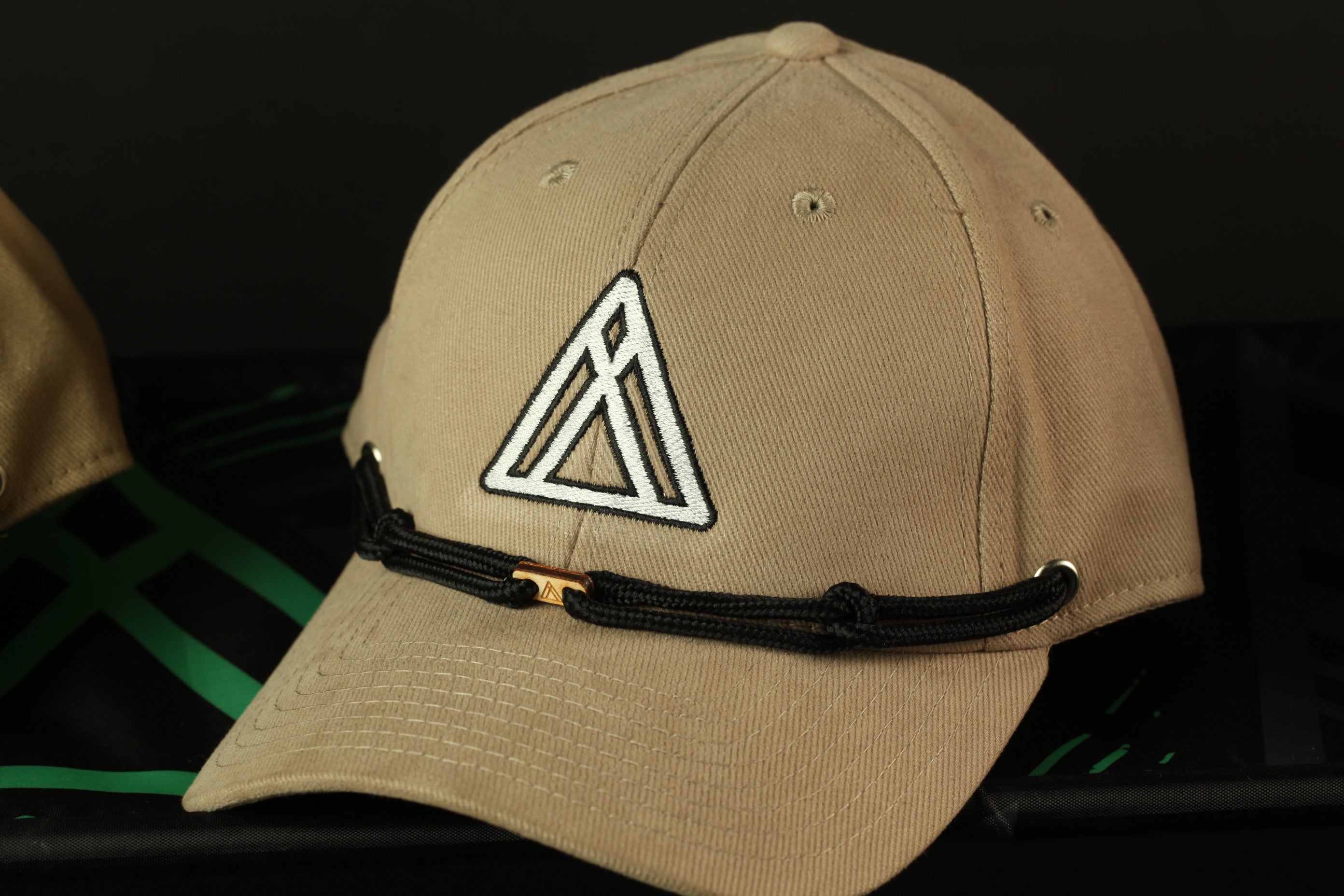 A beige baseball cap with a white triangle logo on the front, resting on a black surface.