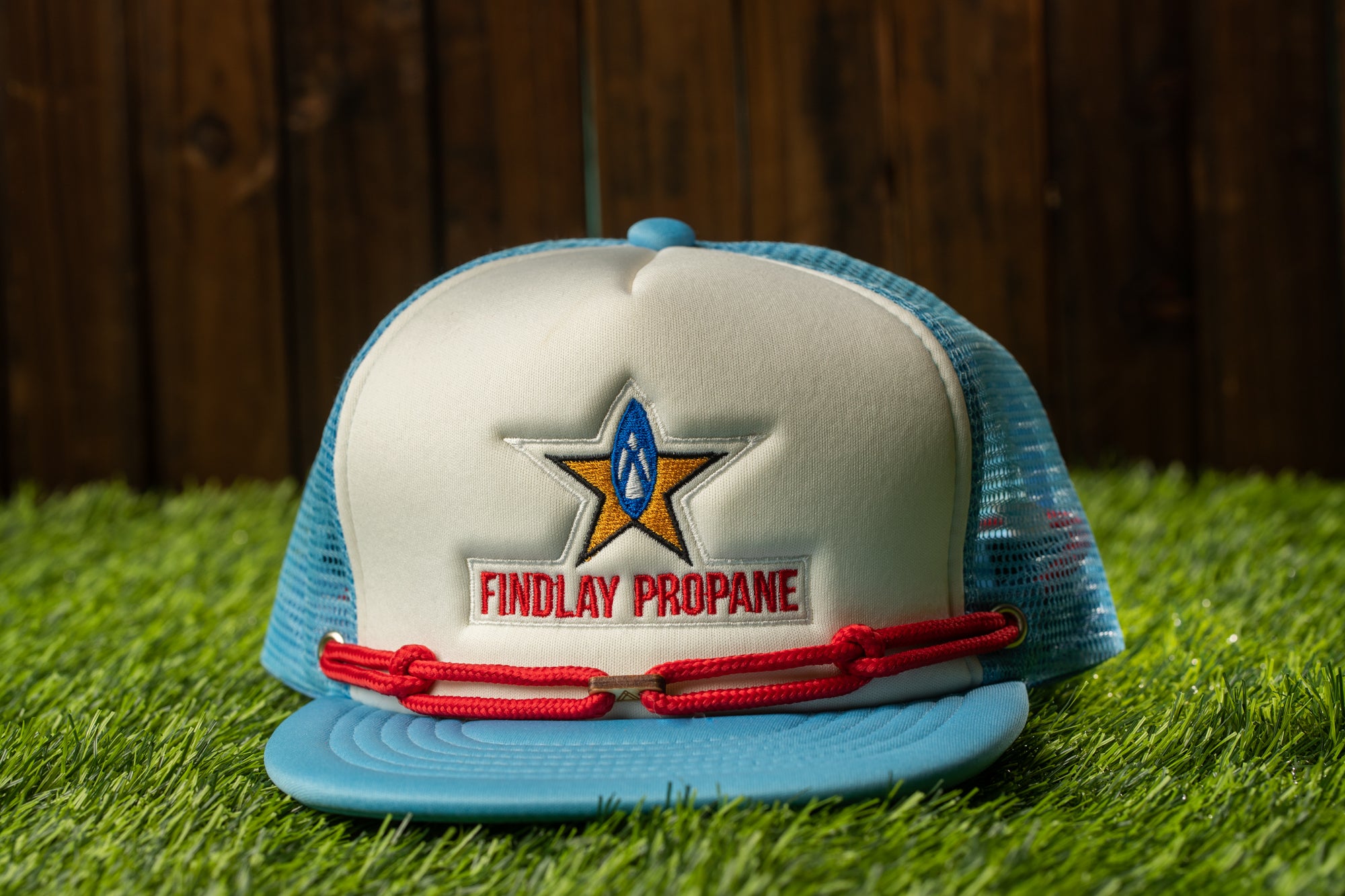 A blue and white baseball cap with a red string and a logo on the front, placed on a grassy surface.
