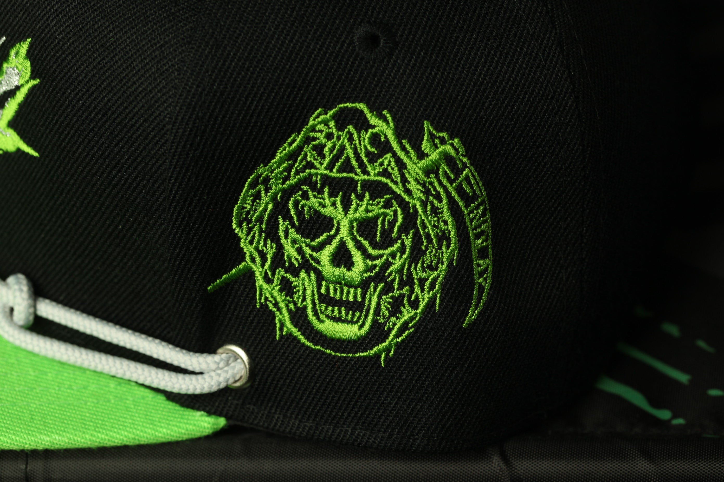 a close-up view of a black baseball cap with a green skull embroidered on it.
