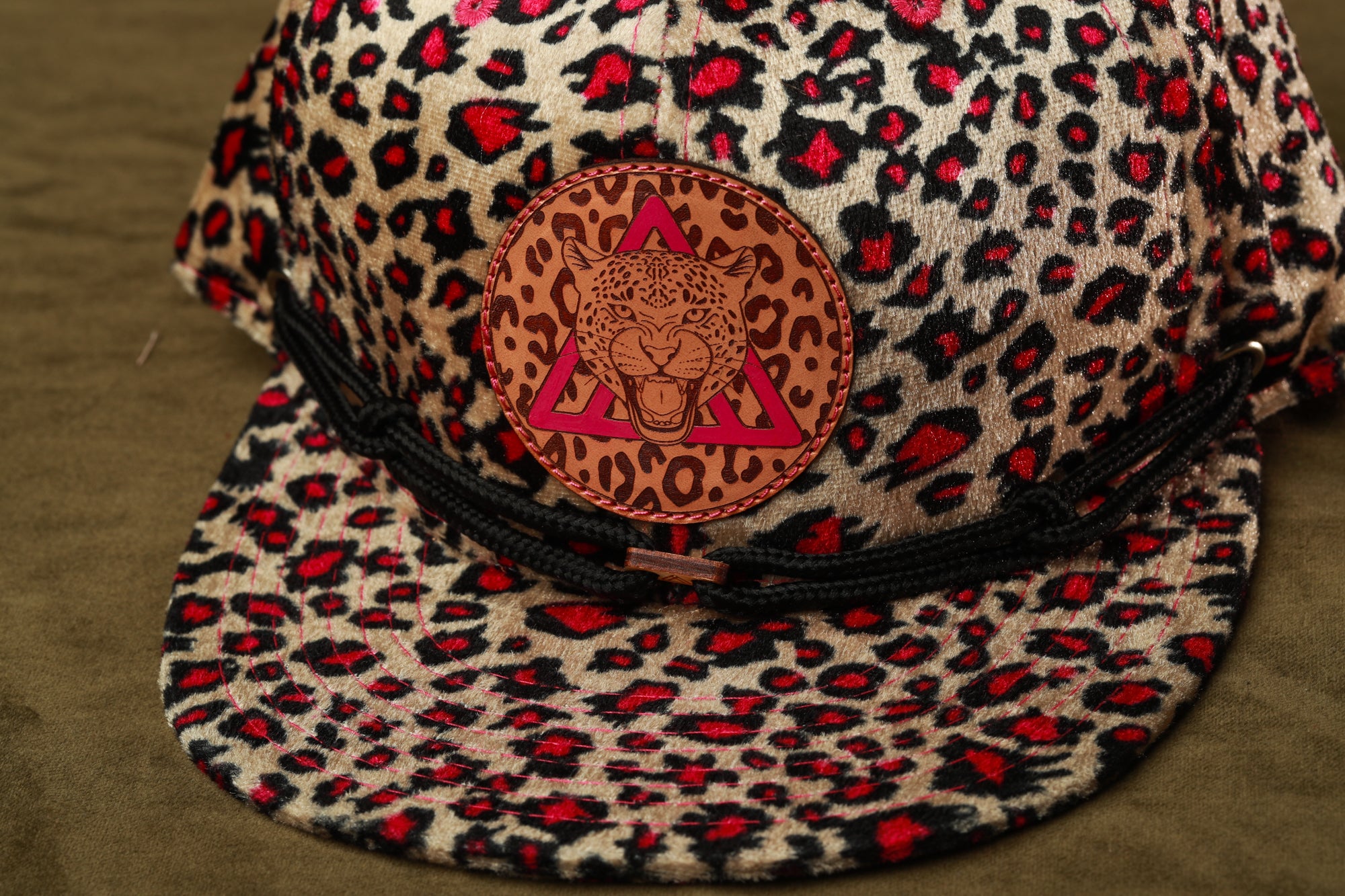 A leopard print baseball cap with a pink triangle logo on the front.