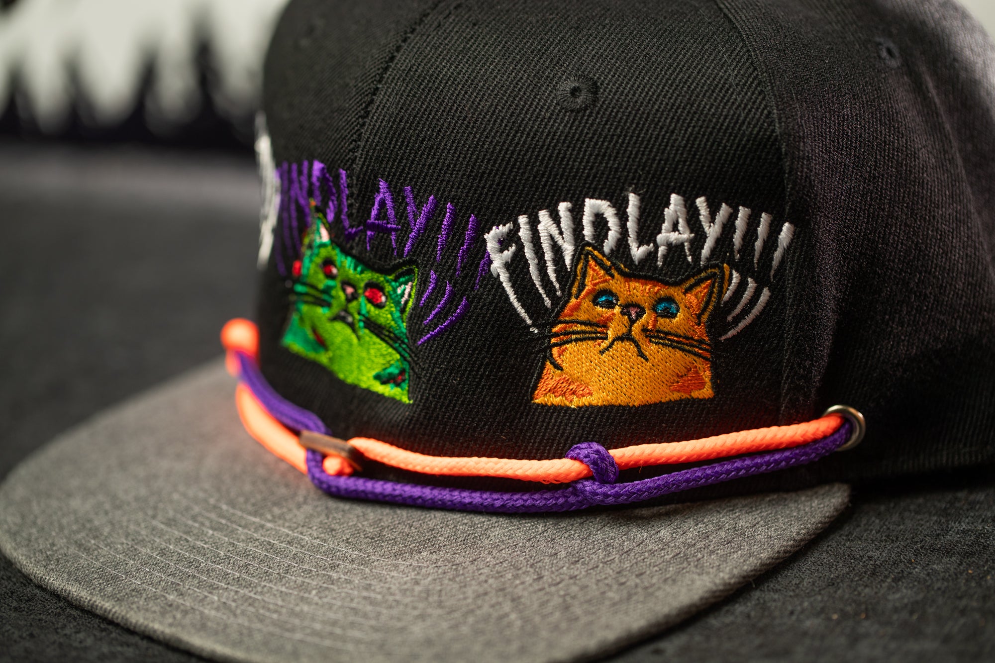 A close-up of a black baseball cap with colorful cat embroidery on the front.