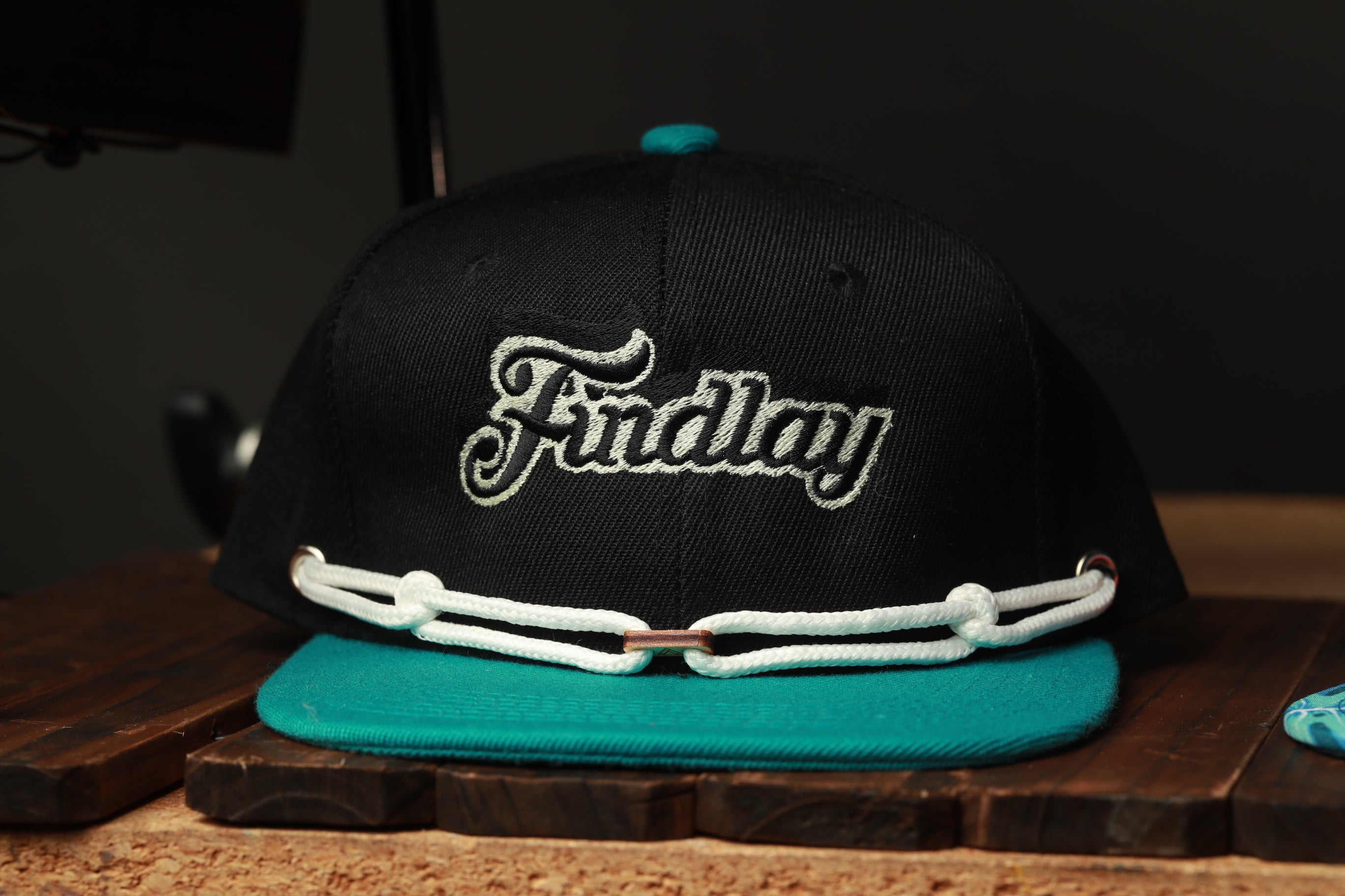 A black baseball cap with the word "Findlay" embroidered on it, placed on a wooden surface.