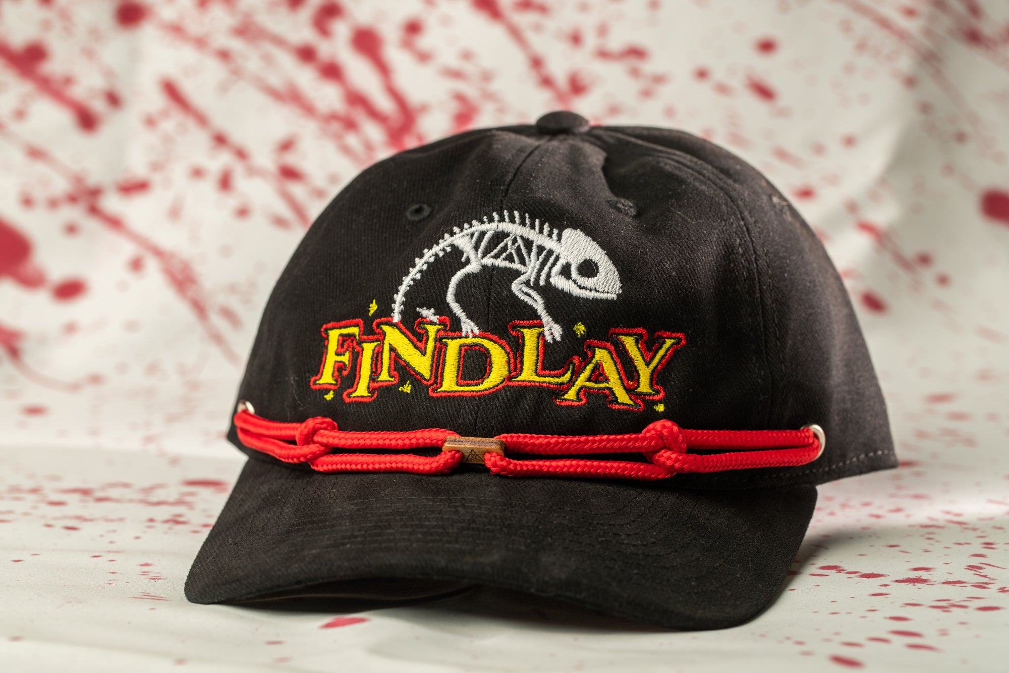 A black baseball cap with a red string and a white and yellow logo that says "FINDlay".