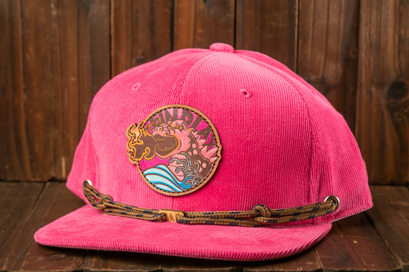 A pink baseball cap with a circular logo on the front, placed on a wooden surface.