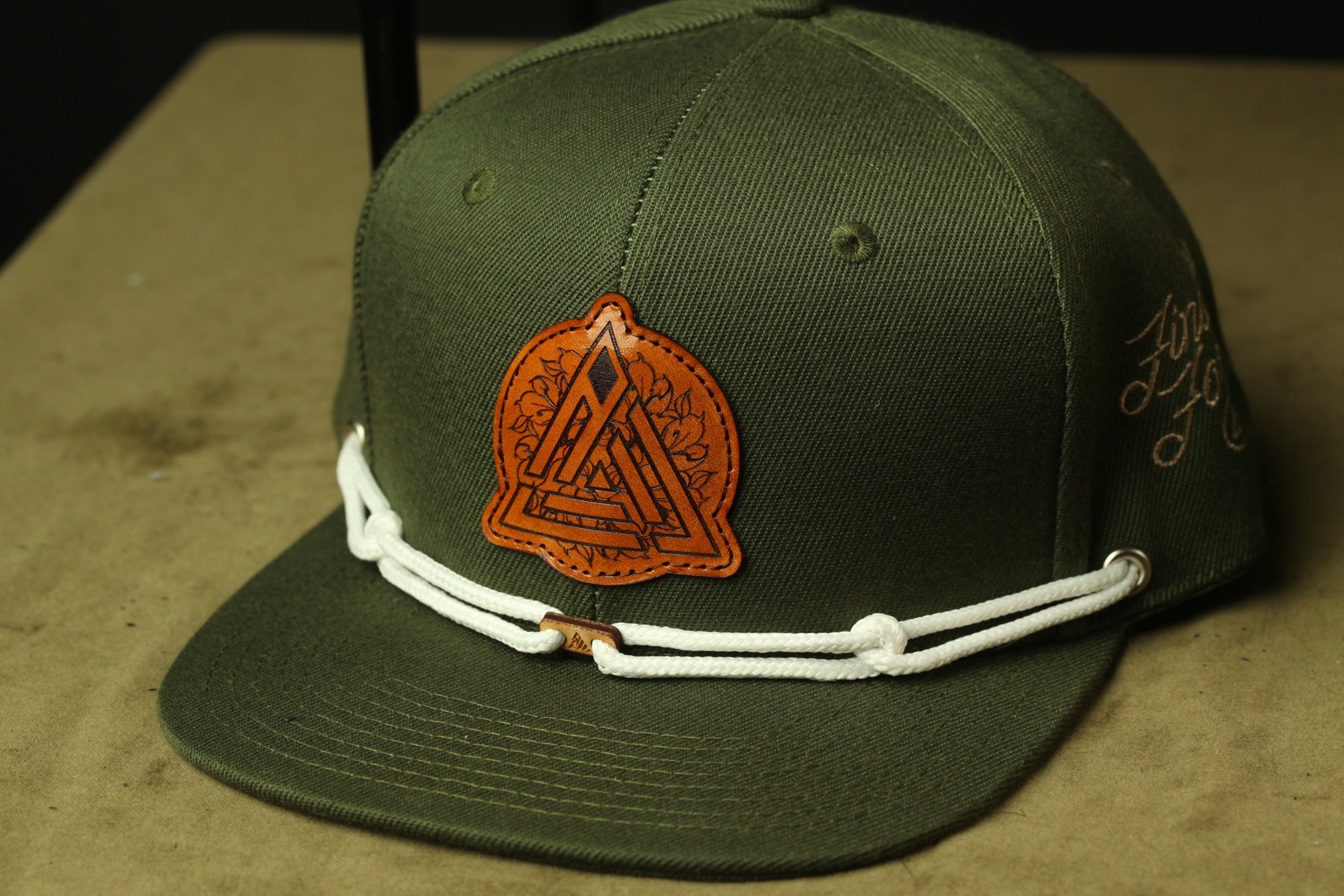 A green baseball cap with a leather patch featuring a geometric design and a white lace trim.
