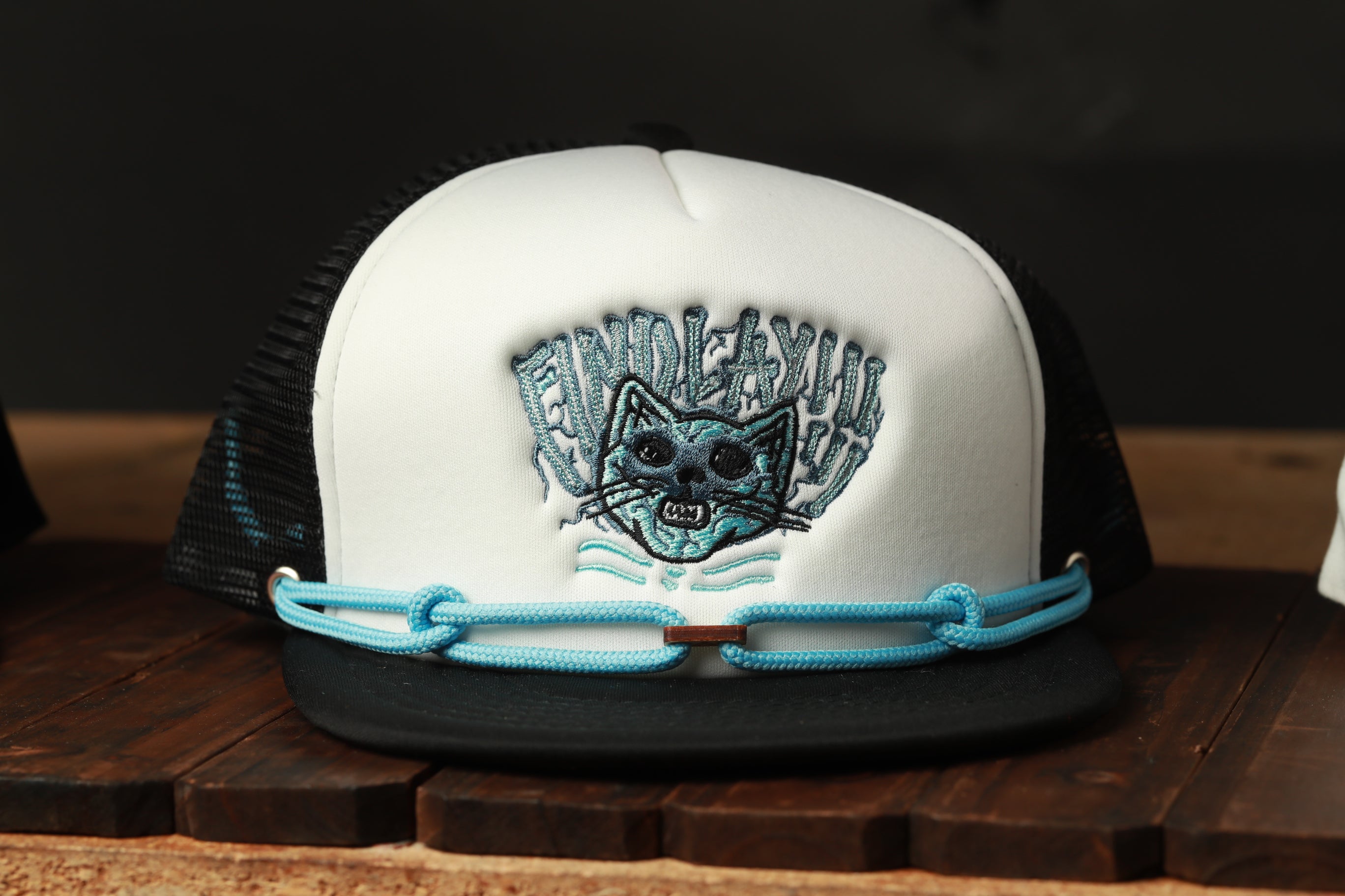 A white baseball cap with a cat embroidered on it, sitting on a wooden surface.