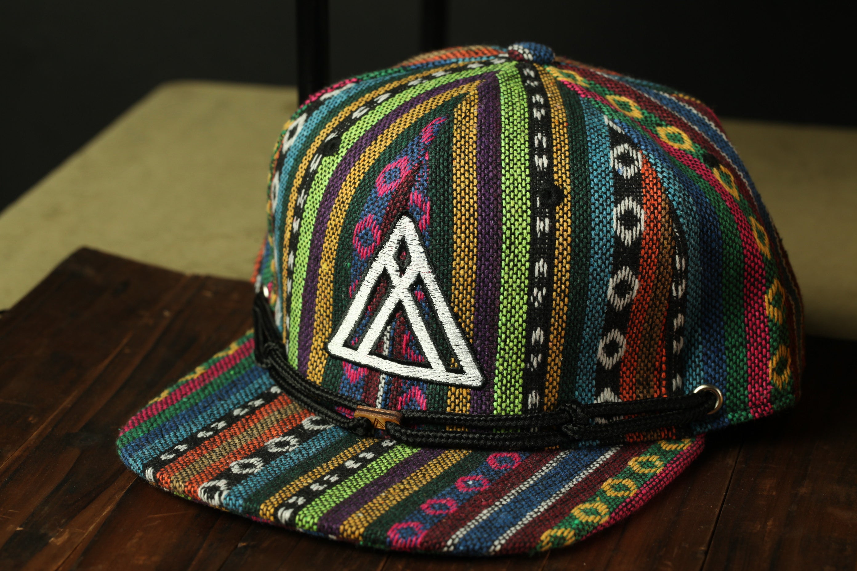 A colorful, patterned baseball cap with a white triangle logo on the front, resting on a wooden surface.