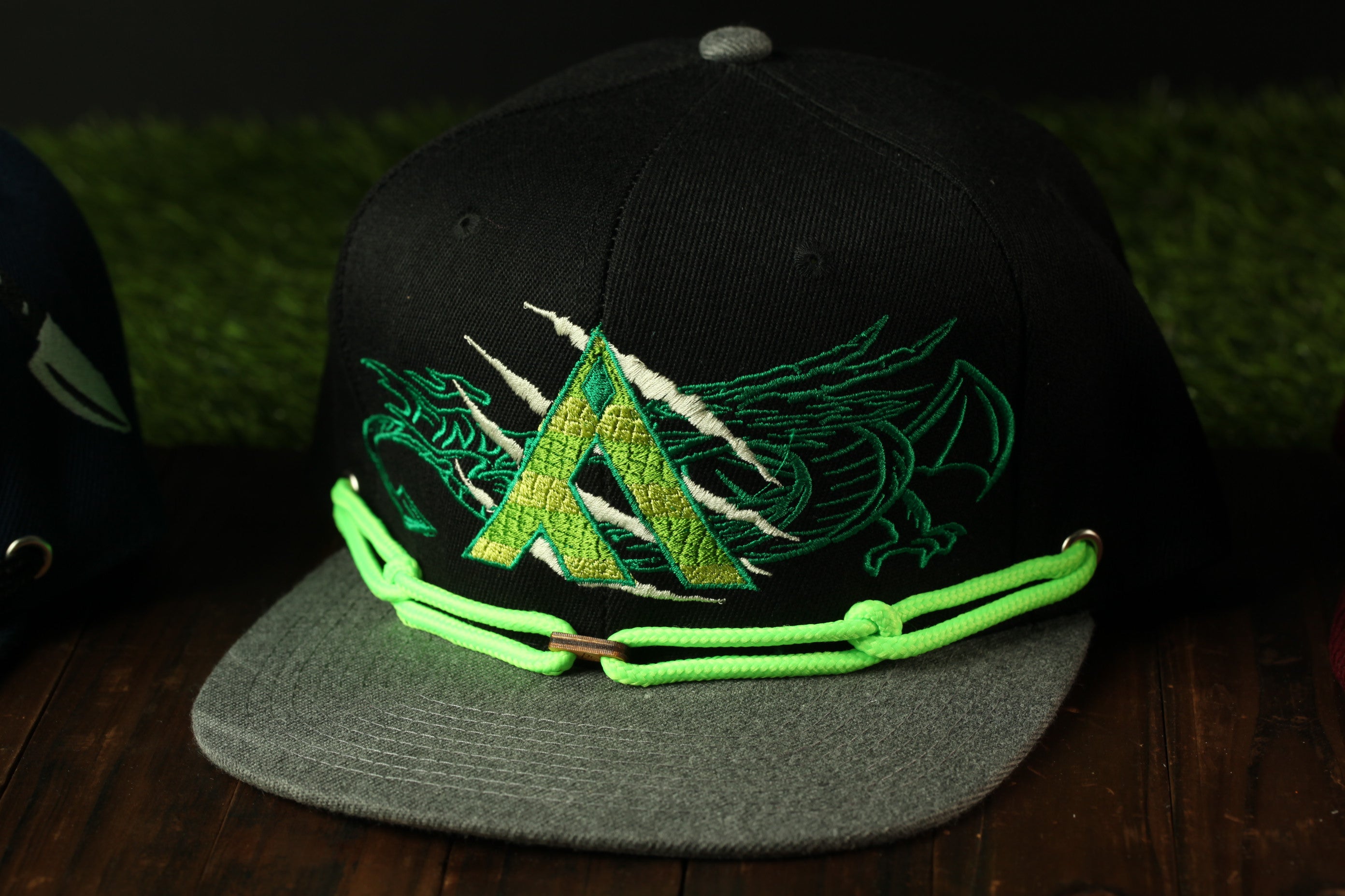 A black baseball cap with a green and yellow dragon design and a neon green chain strap.