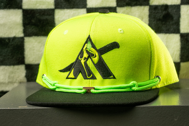 A bright yellow baseball cap with a black logo on it, placed on a black surface against a checkered background.