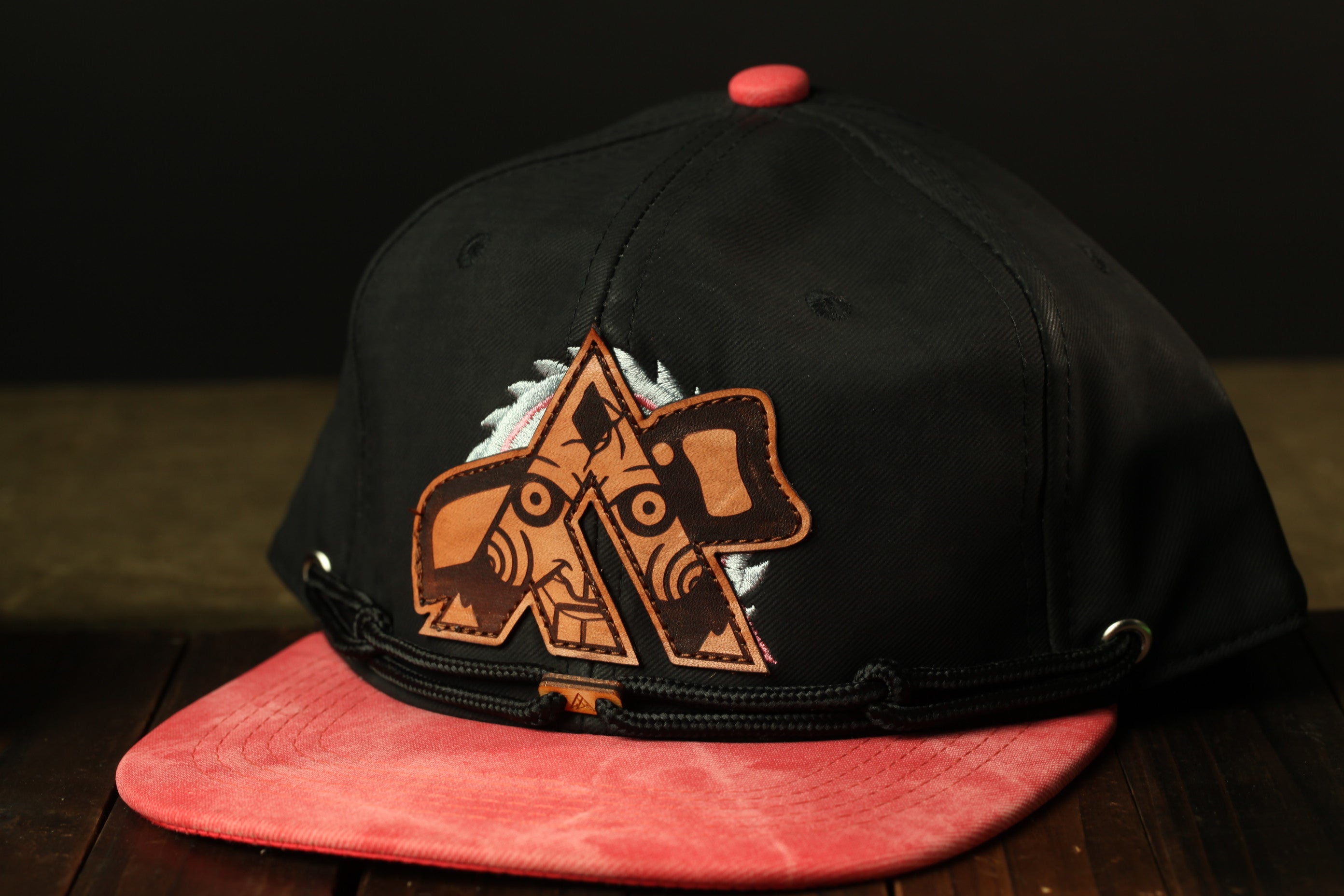 A black baseball cap with a red brim and a unique logo on the front, placed on a wooden surface.