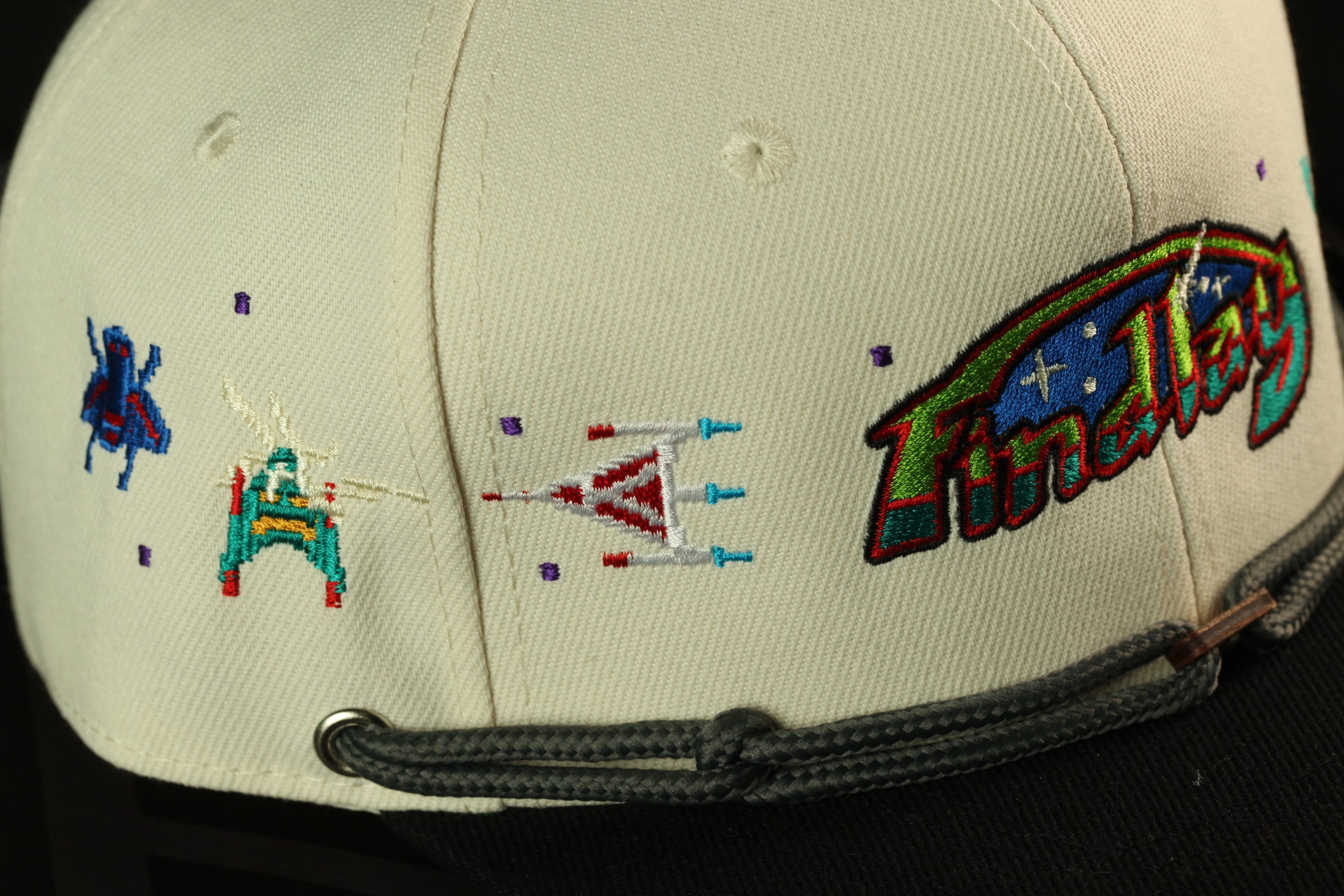 a close-up view of a white baseball cap with colorful embroidered designs, including a space-themed pattern and a small character.