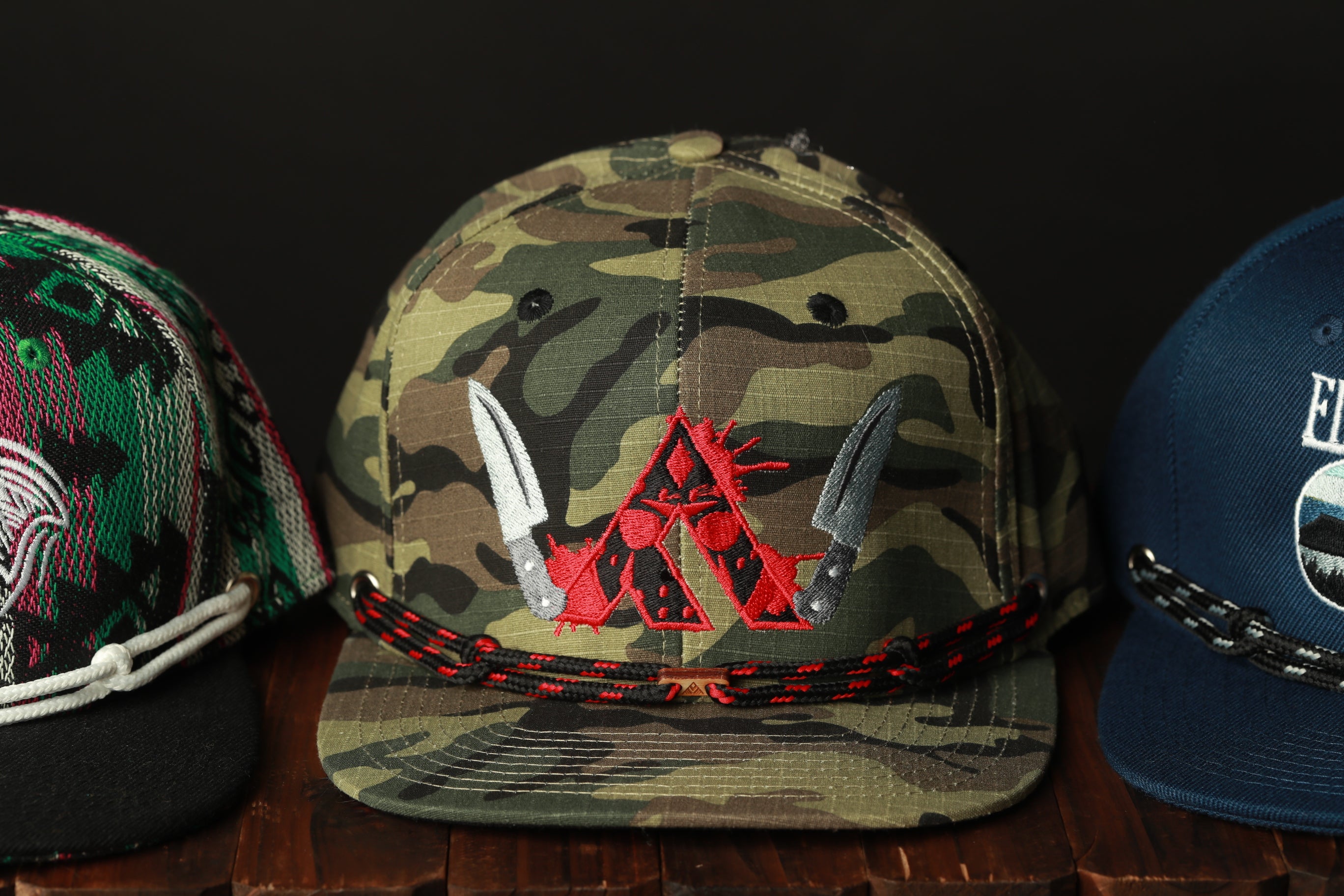 Three baseball caps are displayed on a wooden surface, each with distinct designs and colors.