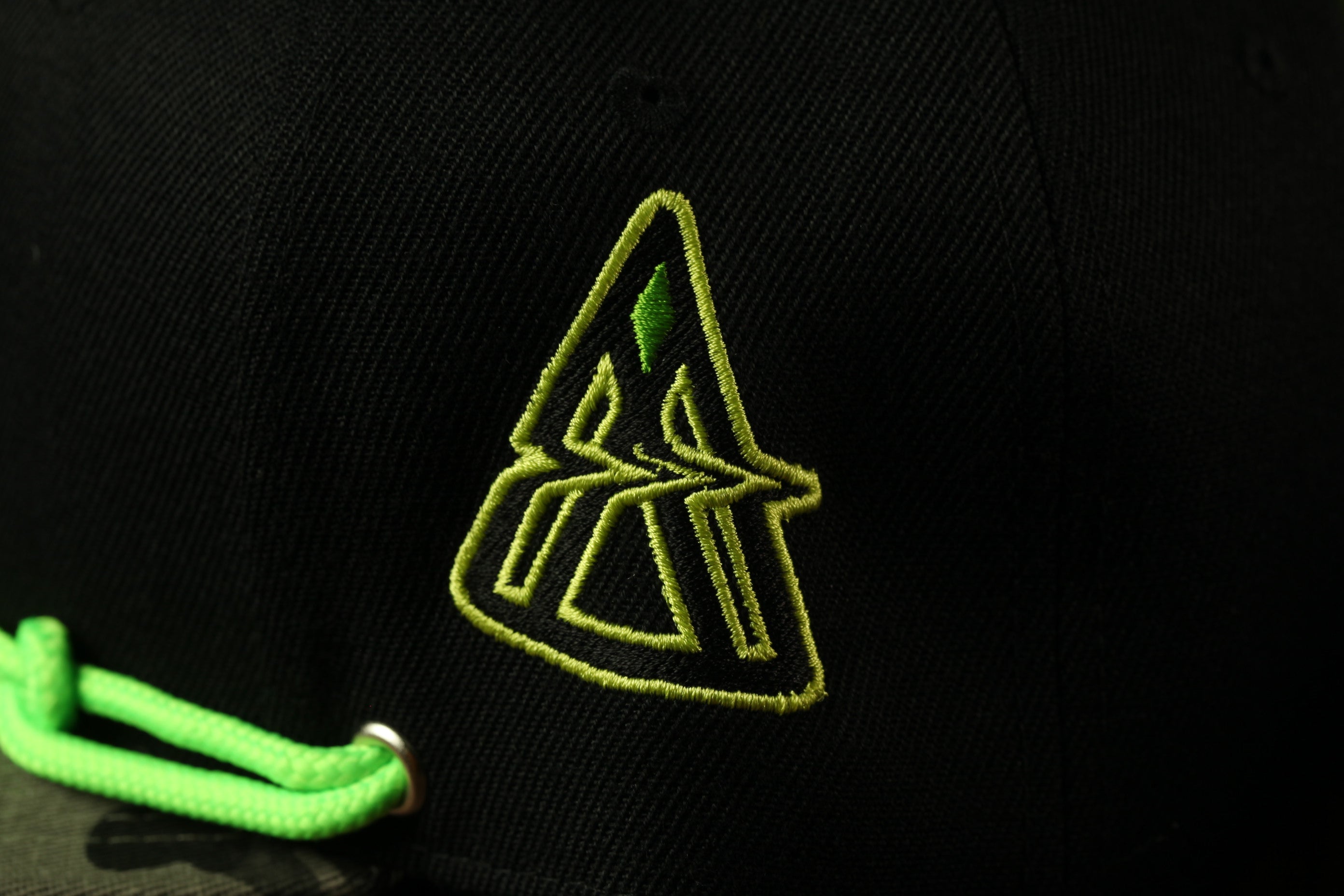A close-up view of a black baseball cap with a green and yellow logo on it.