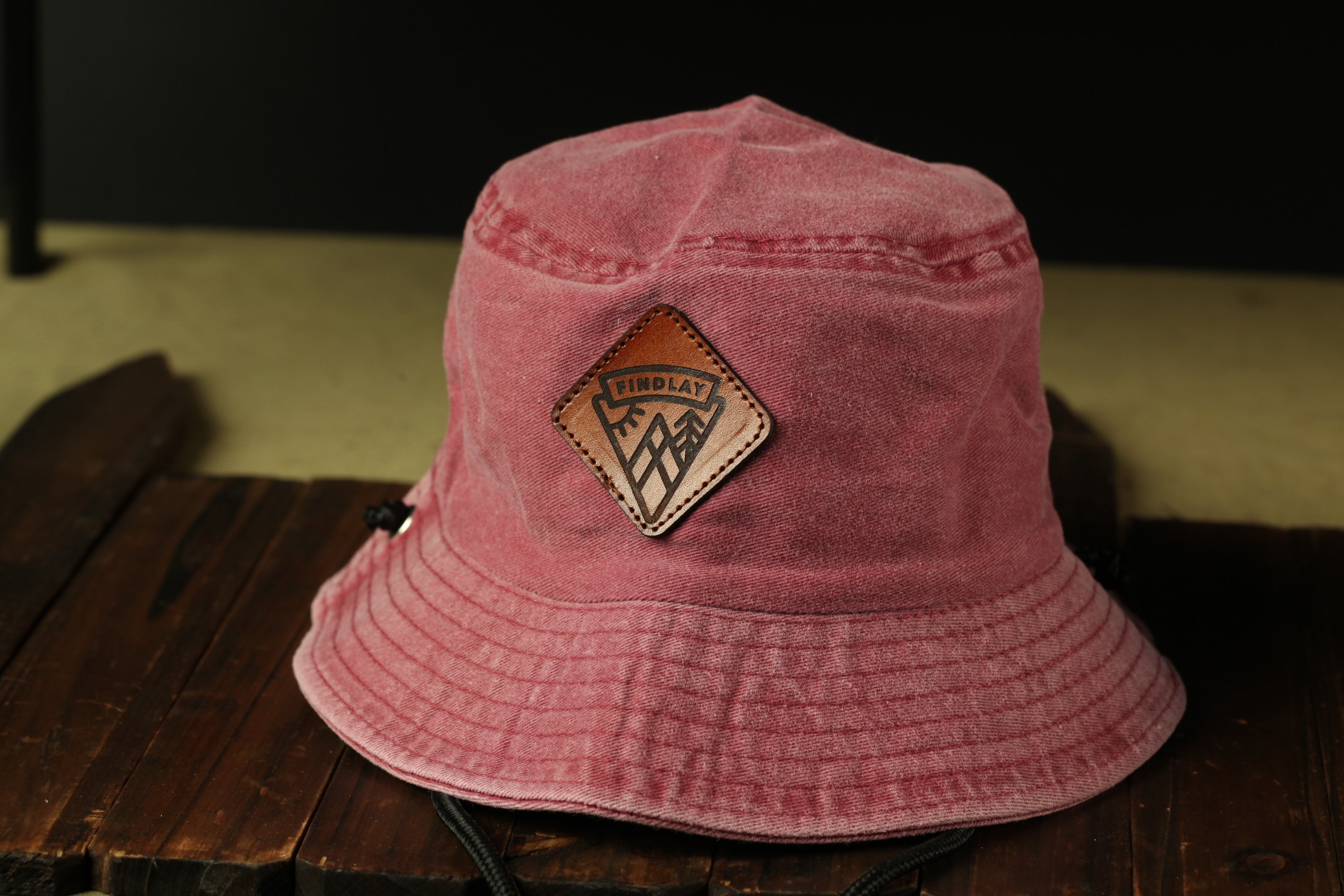 A pink bucket hat with a leather patch on the front, sitting on a wooden surface.