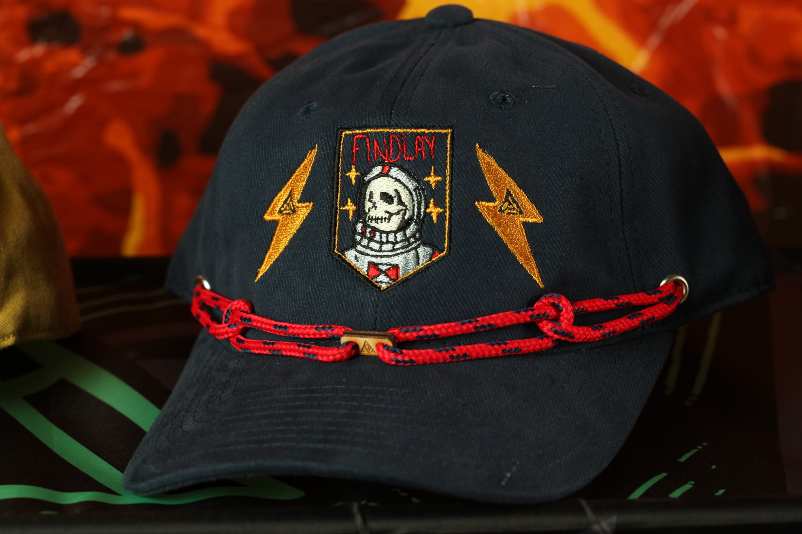 A black baseball cap with a skull and lightning bolt design, and a red string around the brim.