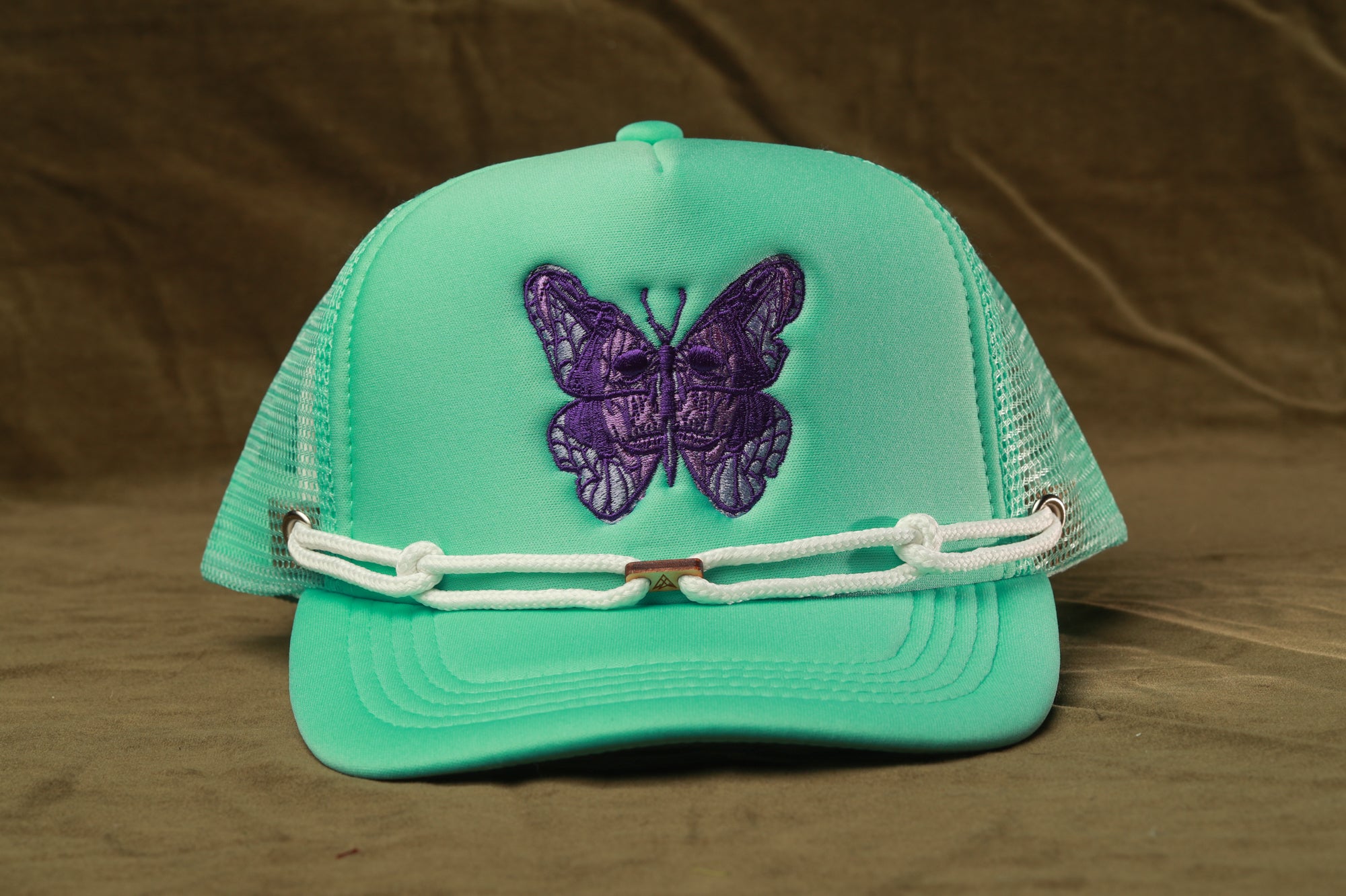 A turquoise baseball cap with a purple butterfly embroidered on it, featuring a white chain strap.