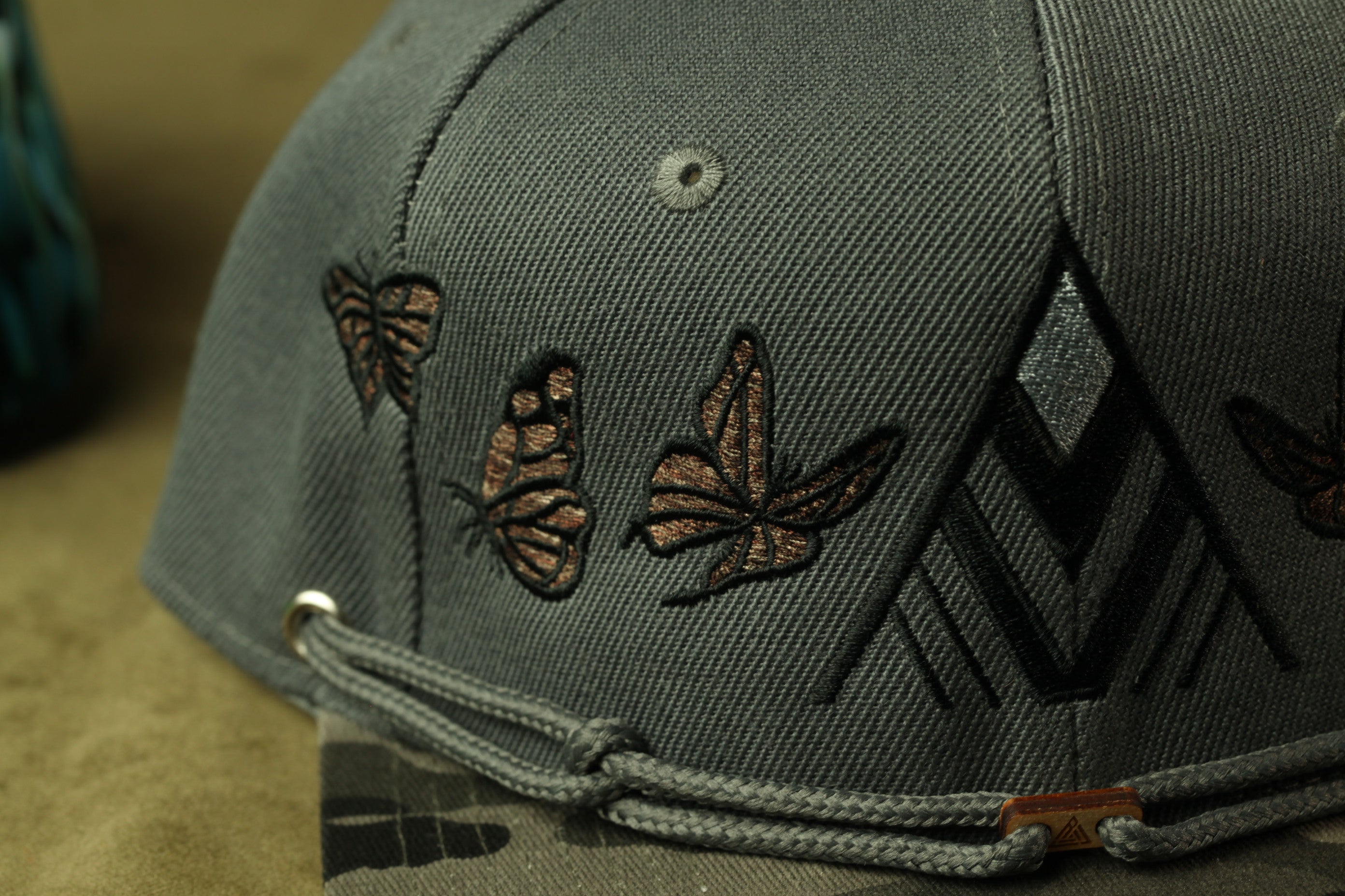 A close-up view of a gray baseball cap with a pattern of butterflies and geometric shapes on the front.