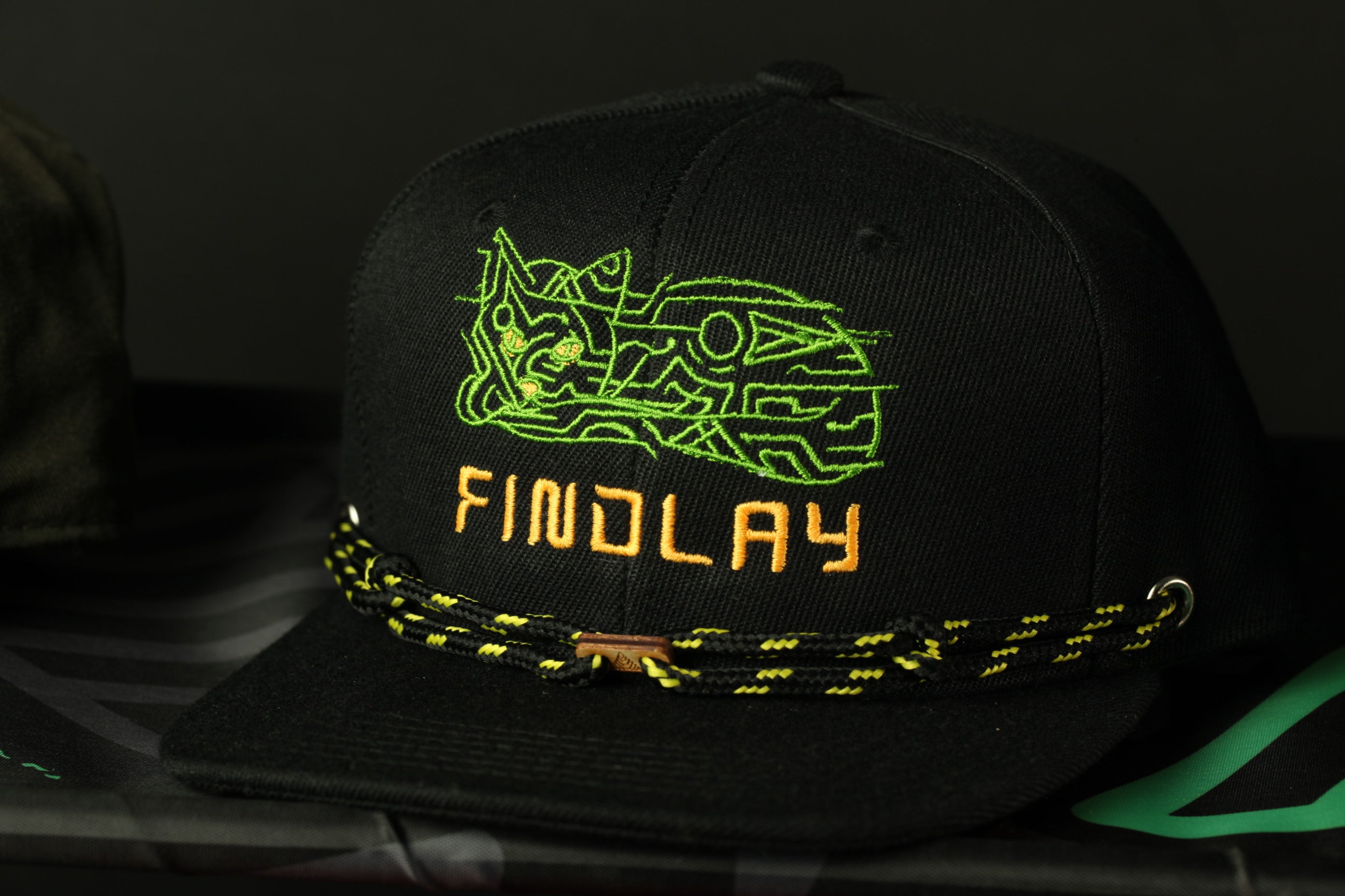 A black baseball cap with a green and yellow embroidered design and the word "FINDLAY" printed on it.