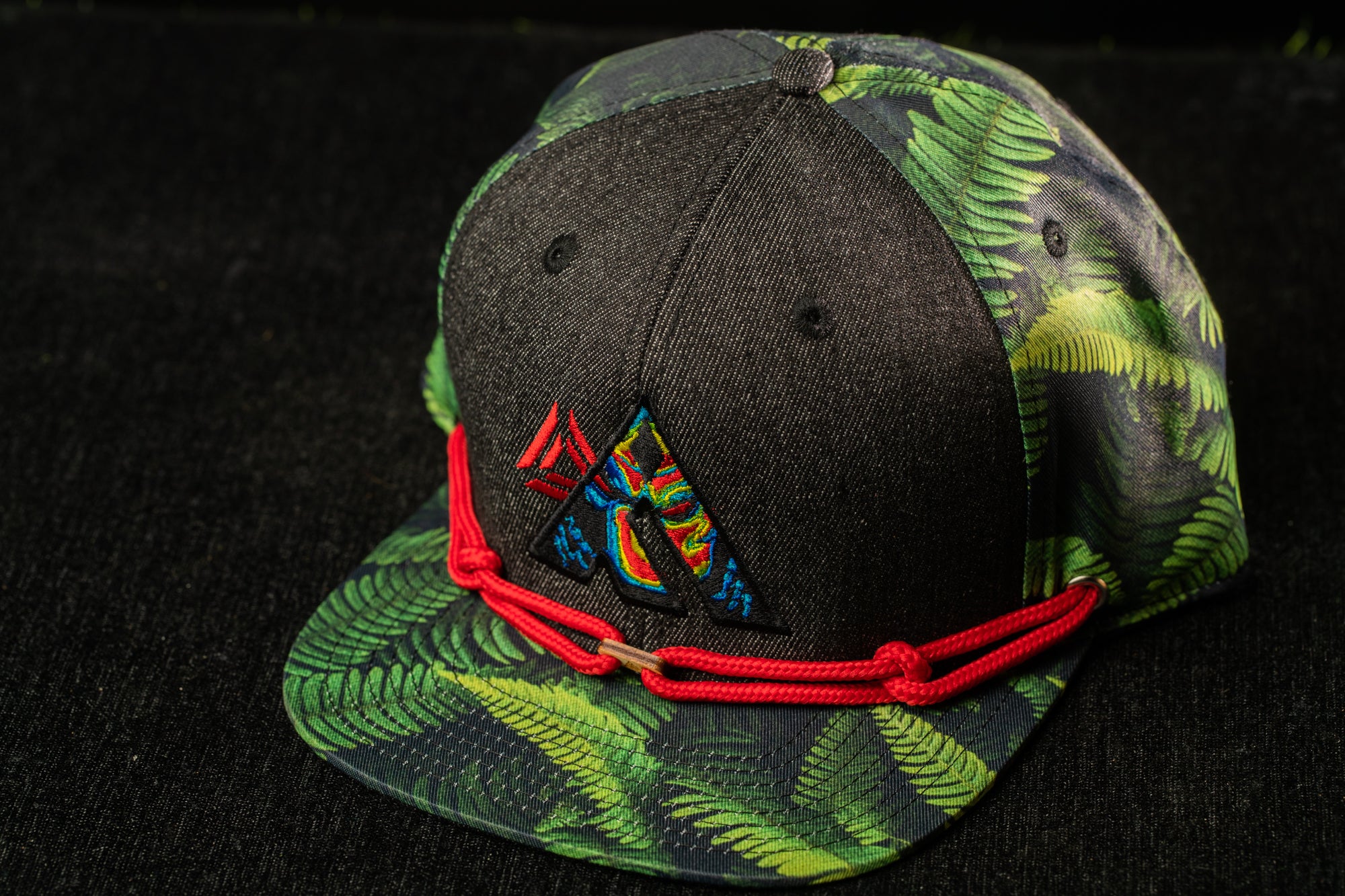 A black baseball cap with a green leaf pattern and a red string around the brim.