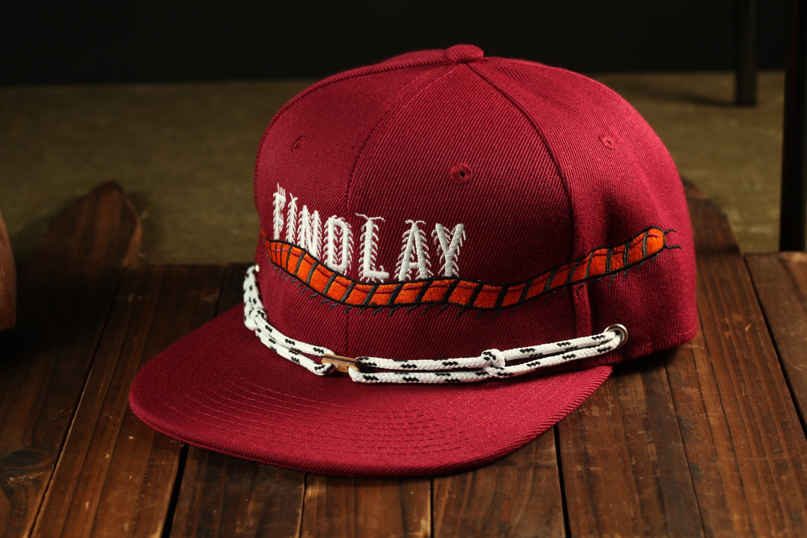 A red baseball cap with the name 'TINDOLAY' embroidered on it, sitting on a wooden surface.