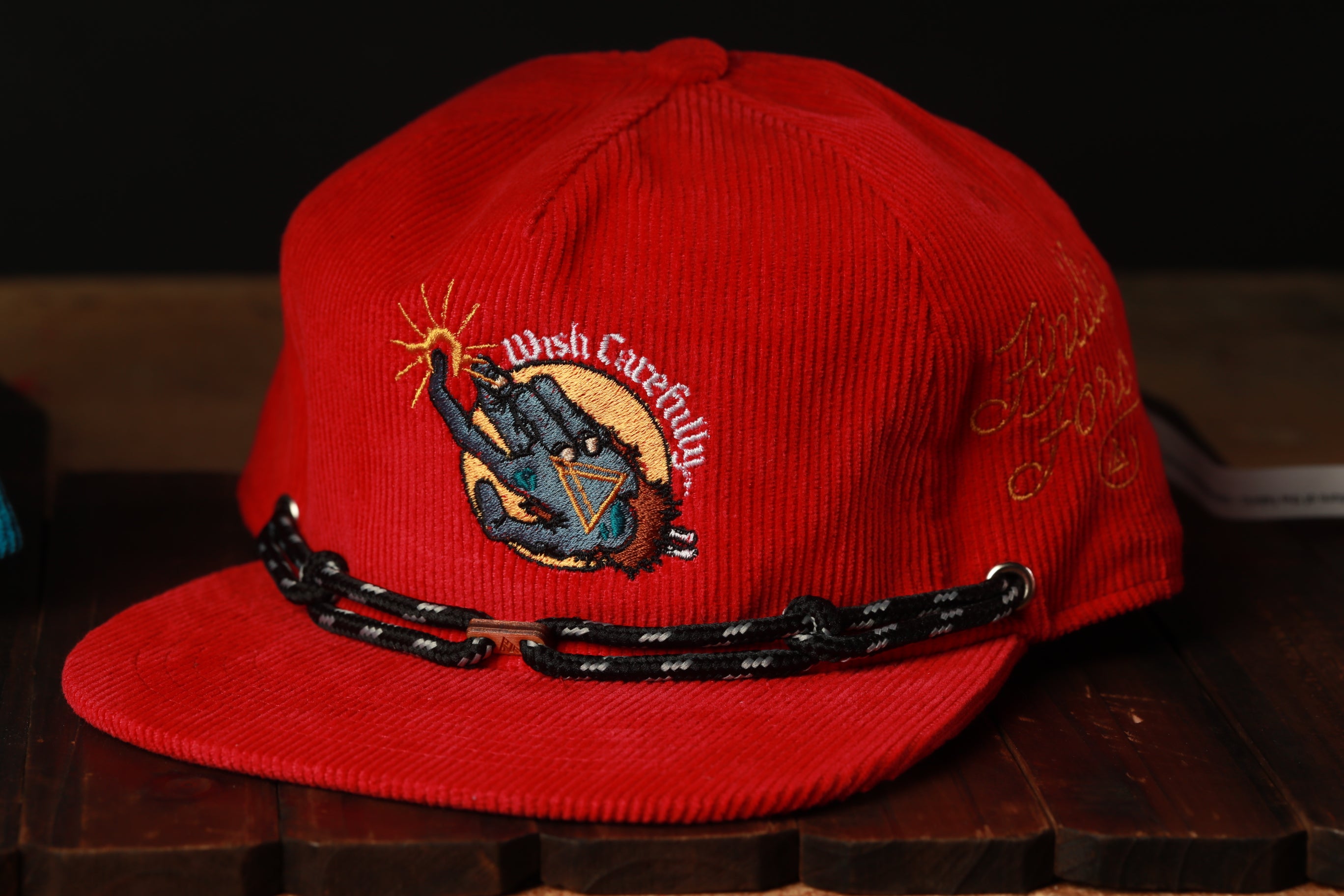 A red baseball cap with a black braided strap and an embroidered design on the front.