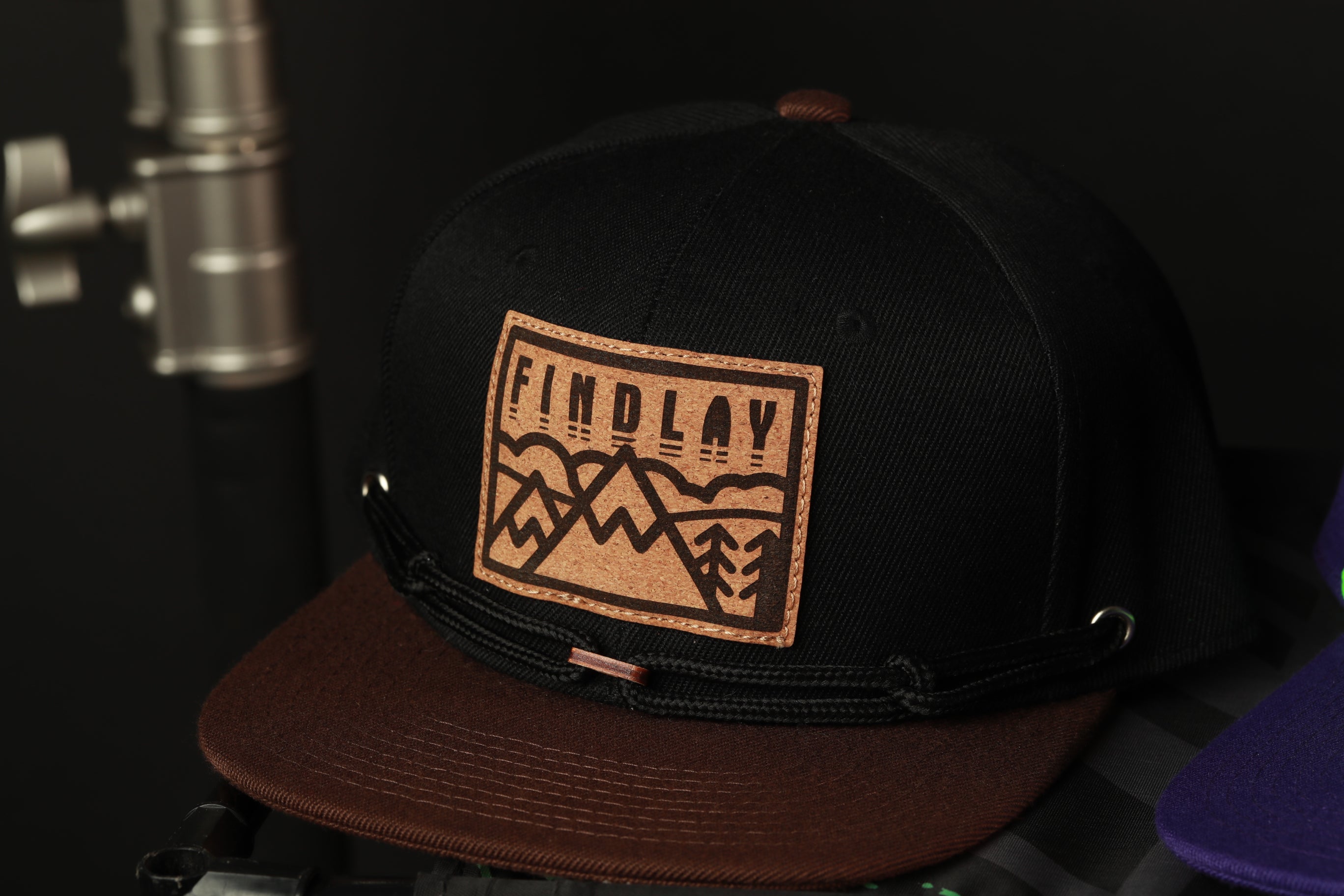 A black baseball cap with a brown leather patch on the front, displaying the word "FINDlay" in a stylized font.