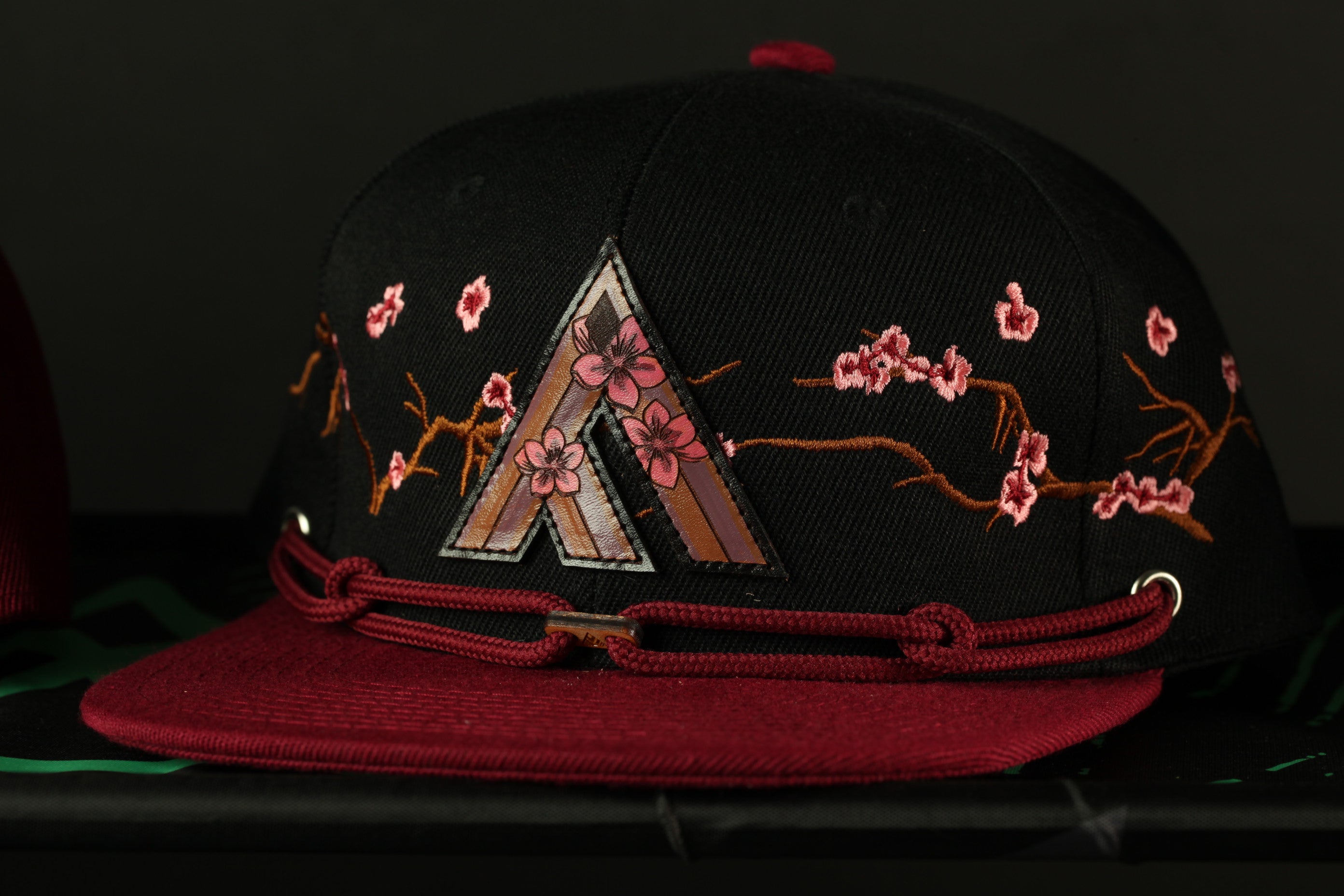 A black baseball cap with a red brim and floral embroidered designs on the front.