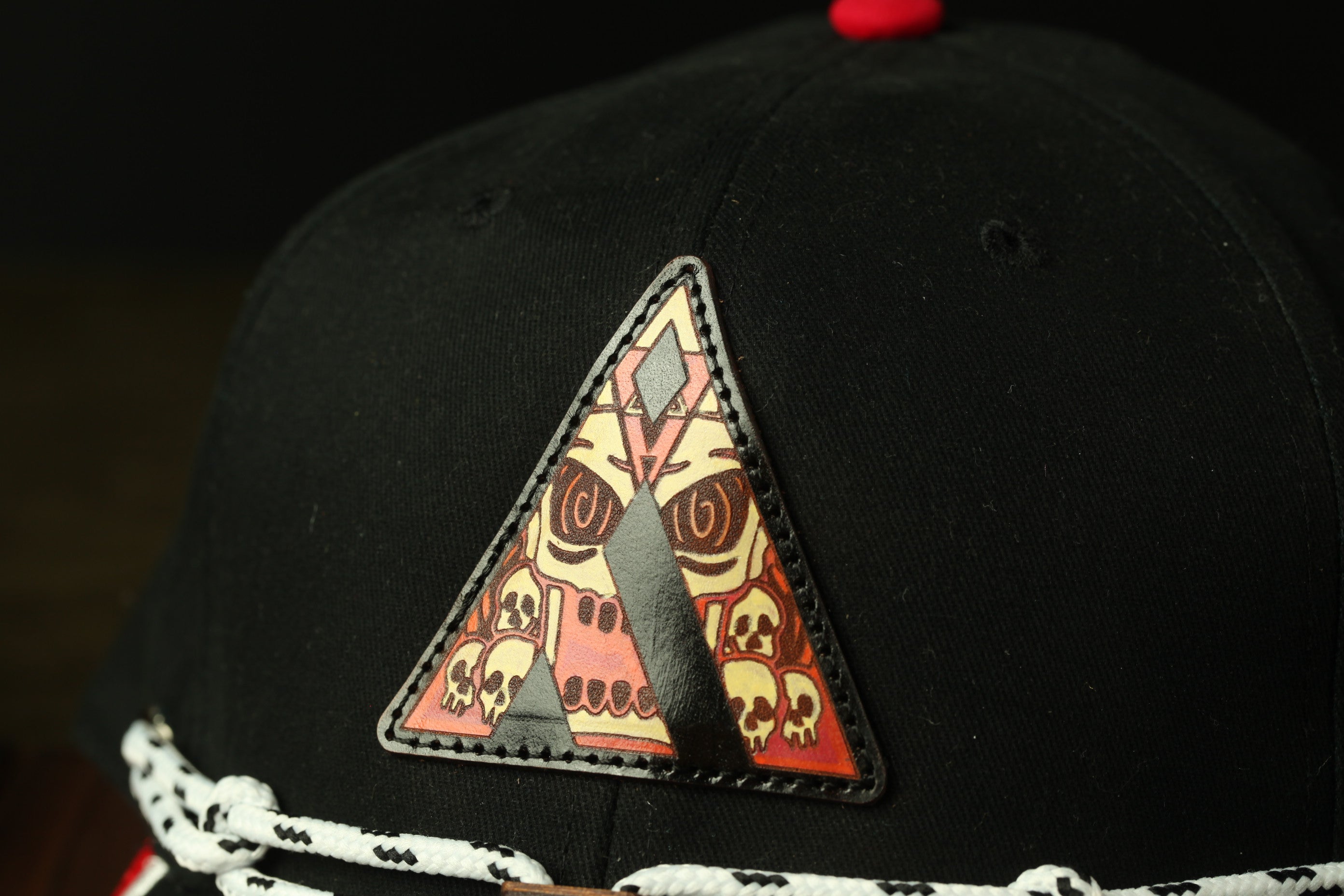 A close-up view of a black baseball cap with a triangular patch featuring a skull design.