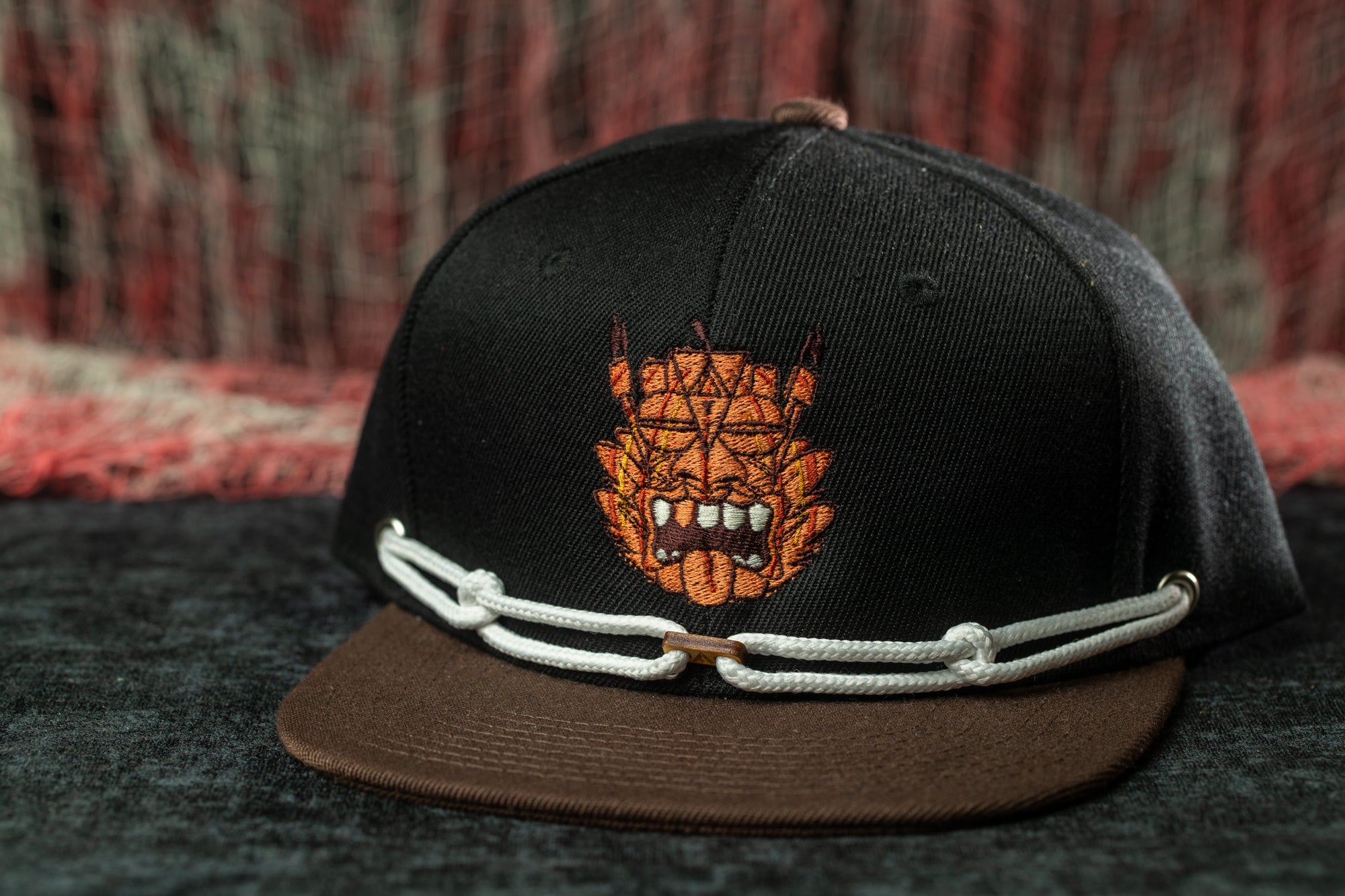 A black baseball cap with an embroidered design on the front, featuring a stylized face with sharp teeth.