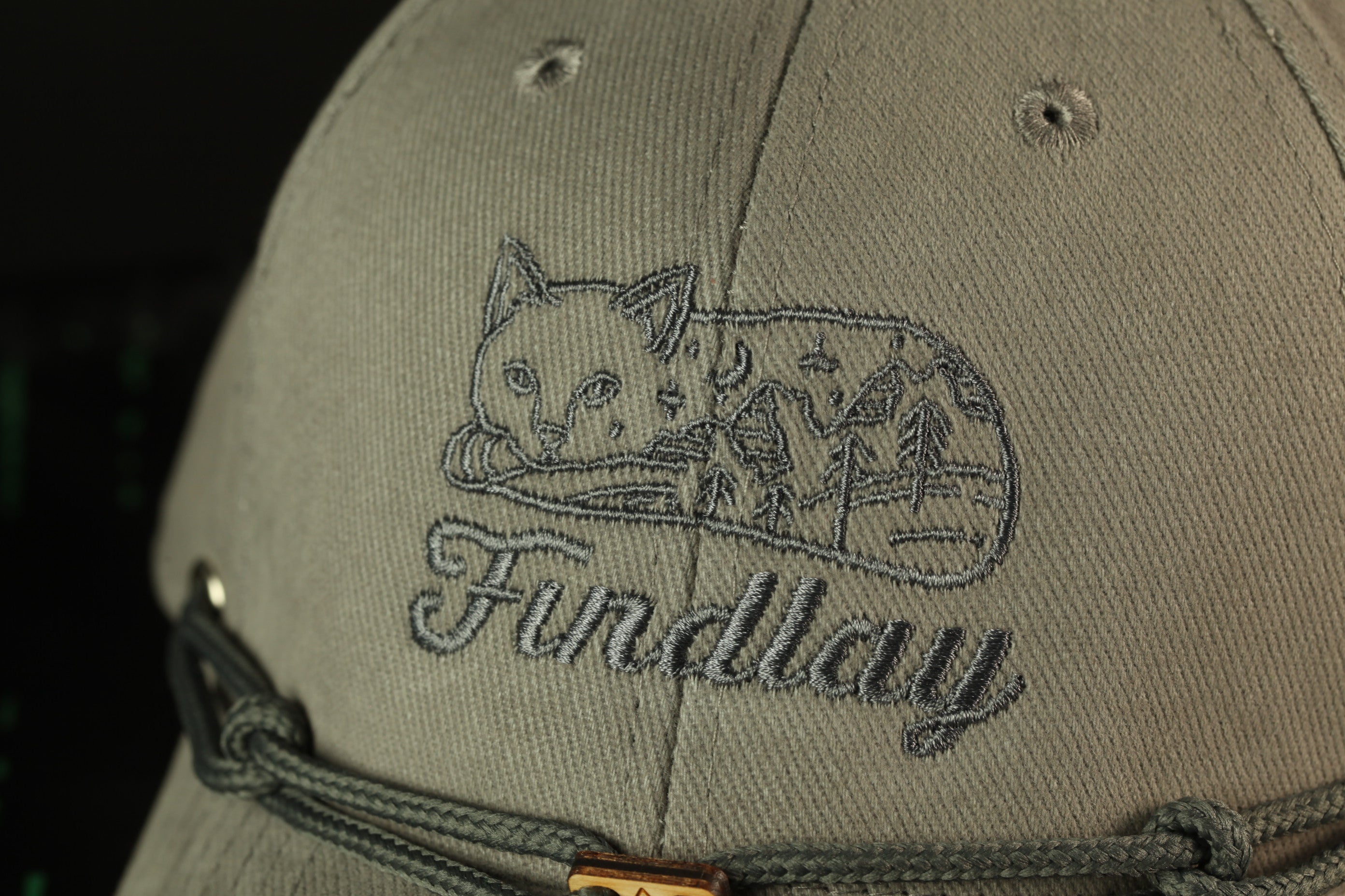 A close-up of a grey baseball cap with a cat embroidered on it, and the word "Fundlay" written below the cat.