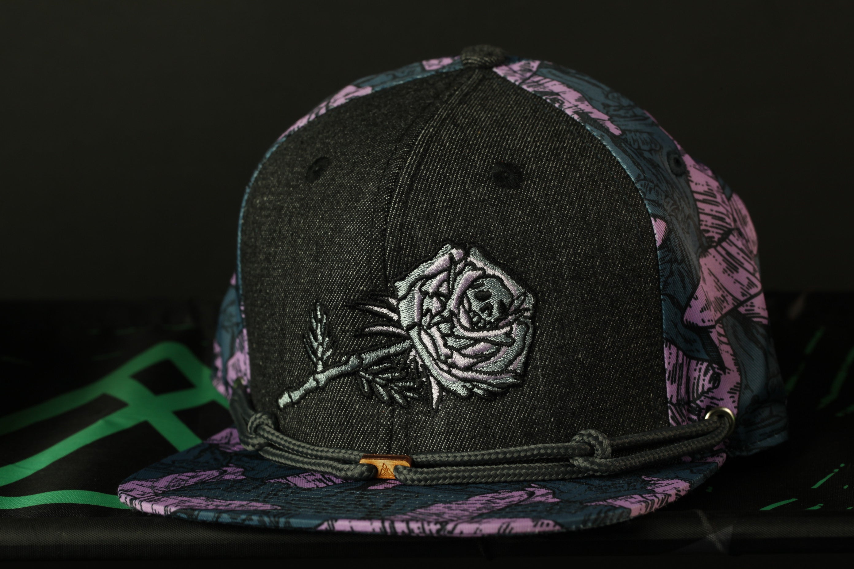 A black baseball cap with a floral pattern and a rose embroidered on the front.