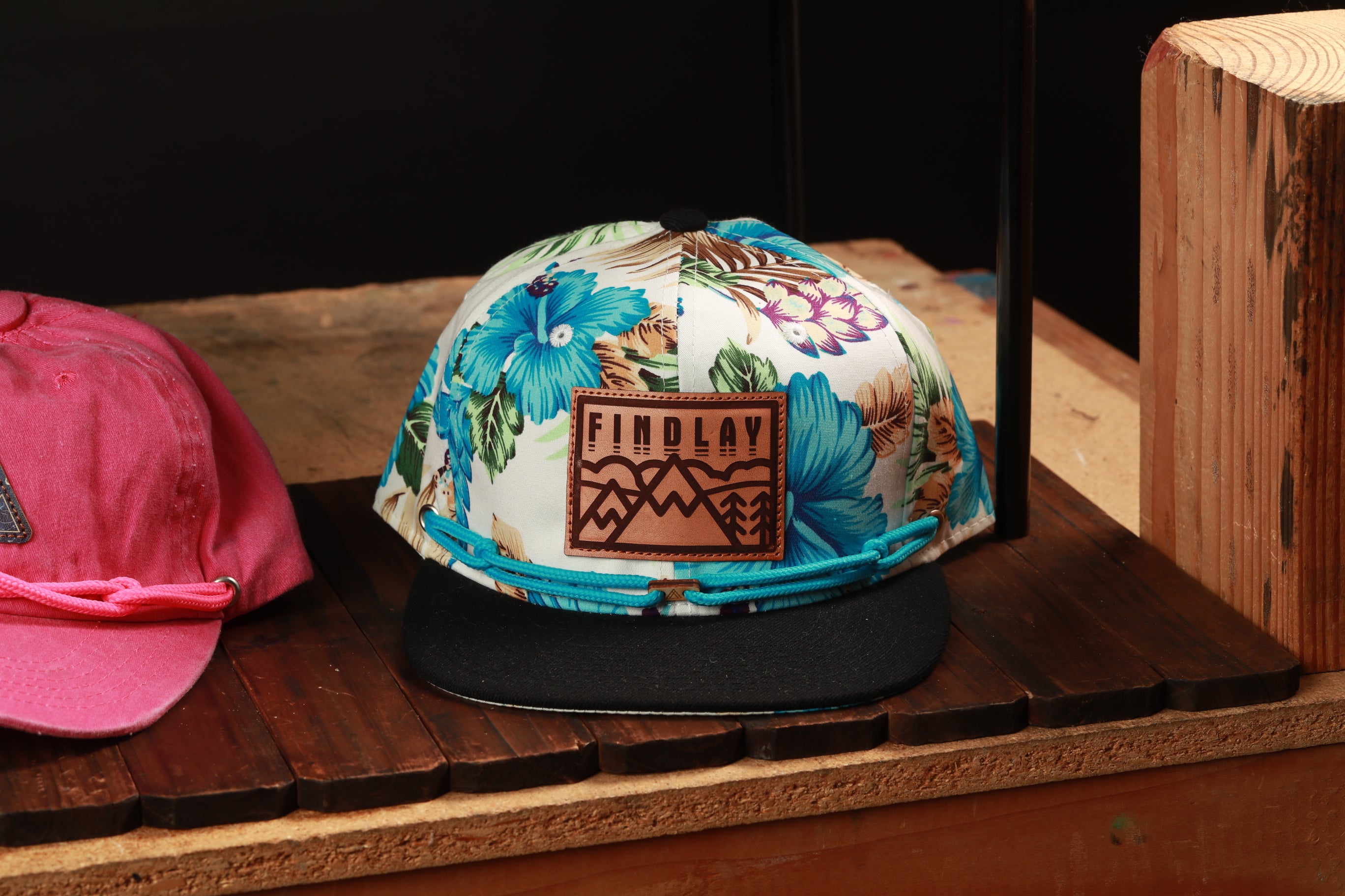 A colorful floral baseball cap with a leather patch on the front, displayed on a wooden surface.