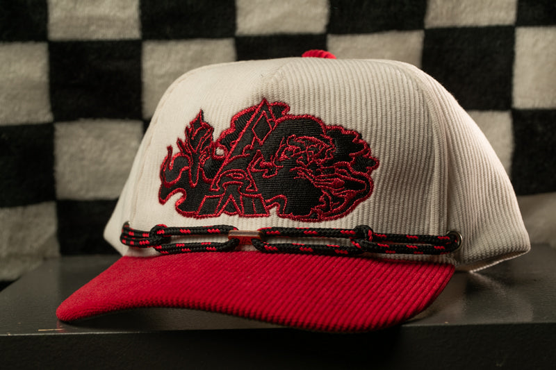 A white baseball cap with a red brim and a black and red embroidered logo on the front, sitting on a black surface against a checkered background.