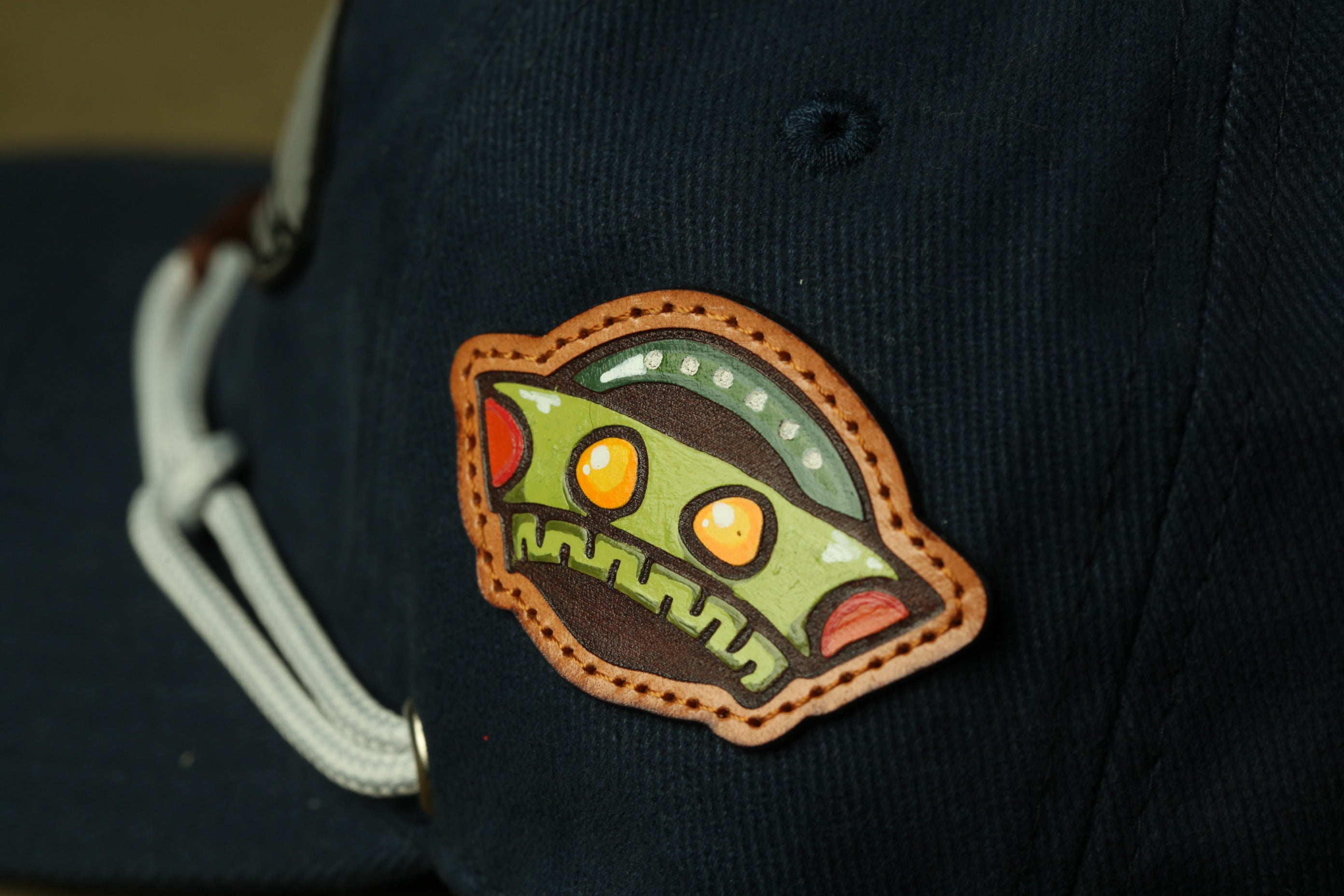 A close-up view of a dark-colored baseball cap with a unique, colorful patch featuring a cartoon-like alien face design.