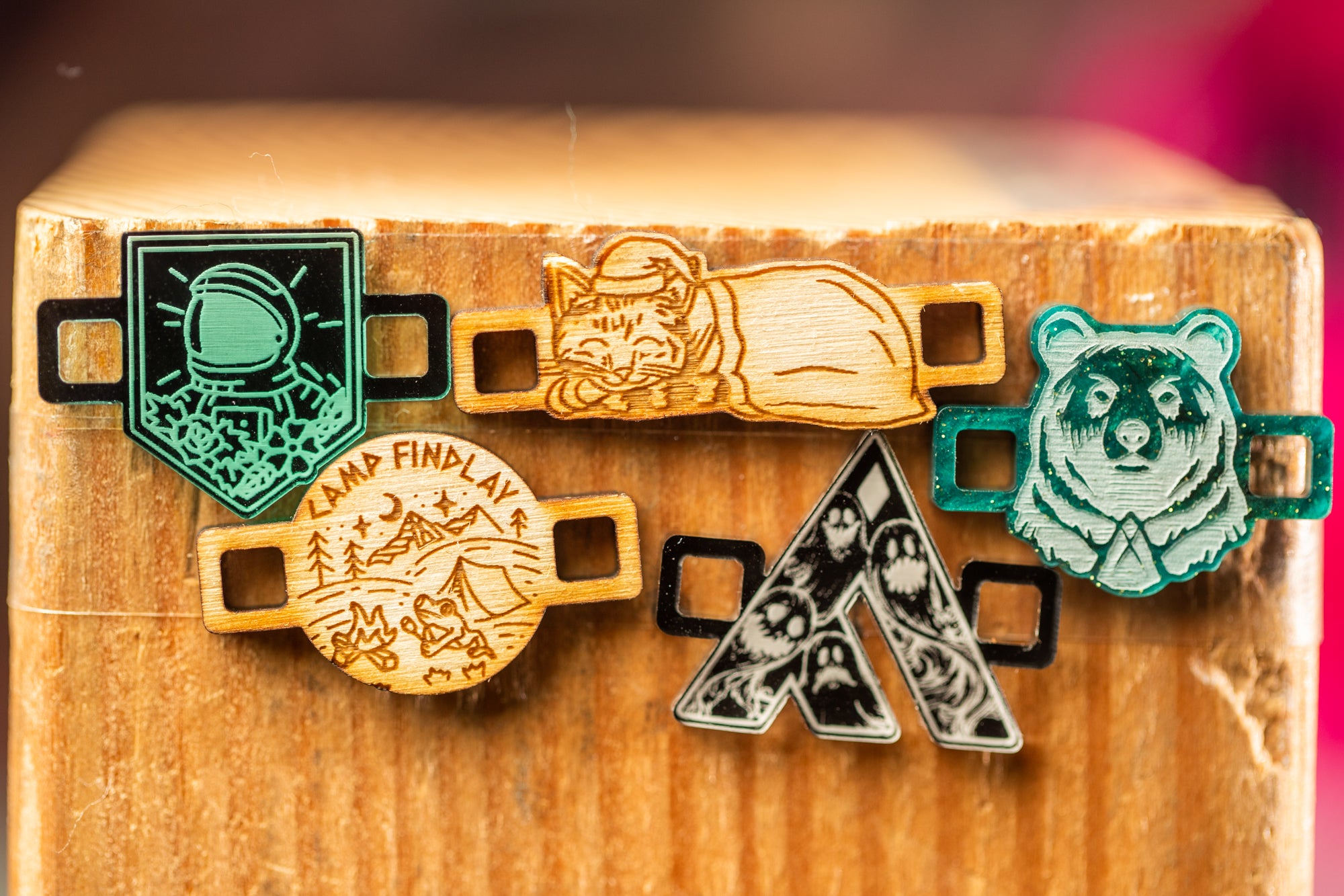 a collection of five wooden badges or charms, each with a unique design, displayed on a wooden surface.