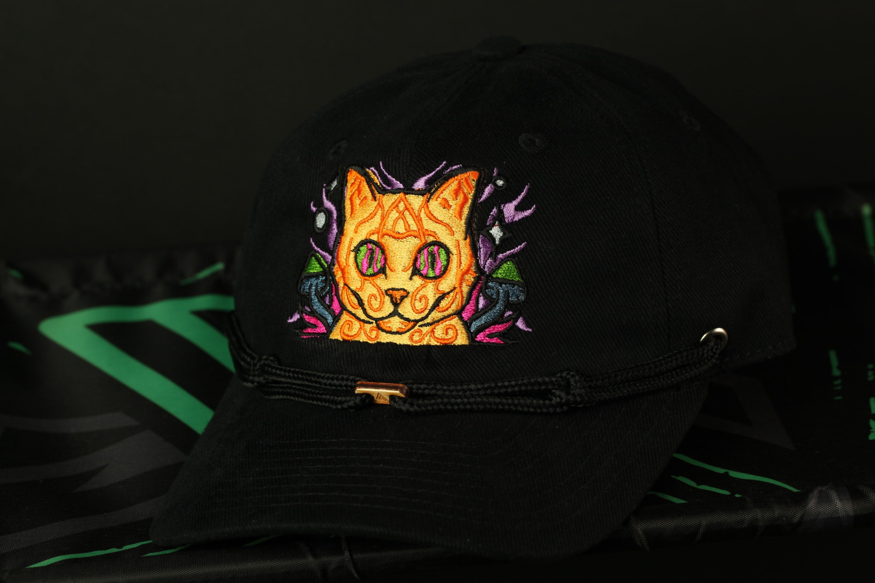 A black baseball cap with a colorful cat embroidered on it, featuring a stylized design and a gold-colored buckle.