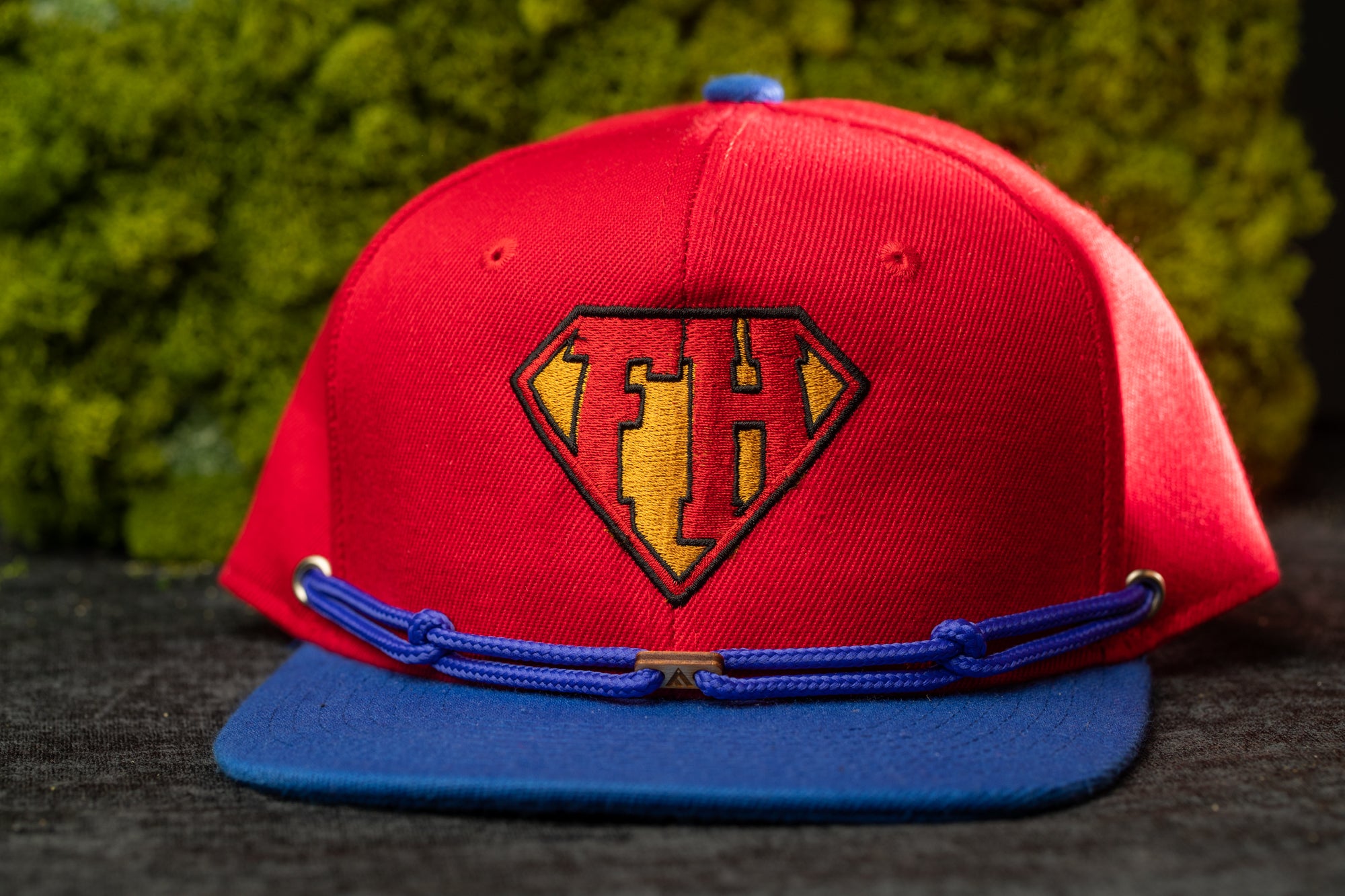 A red baseball cap with a blue brim and a yellow and red logo on the front, placed on a dark surface.