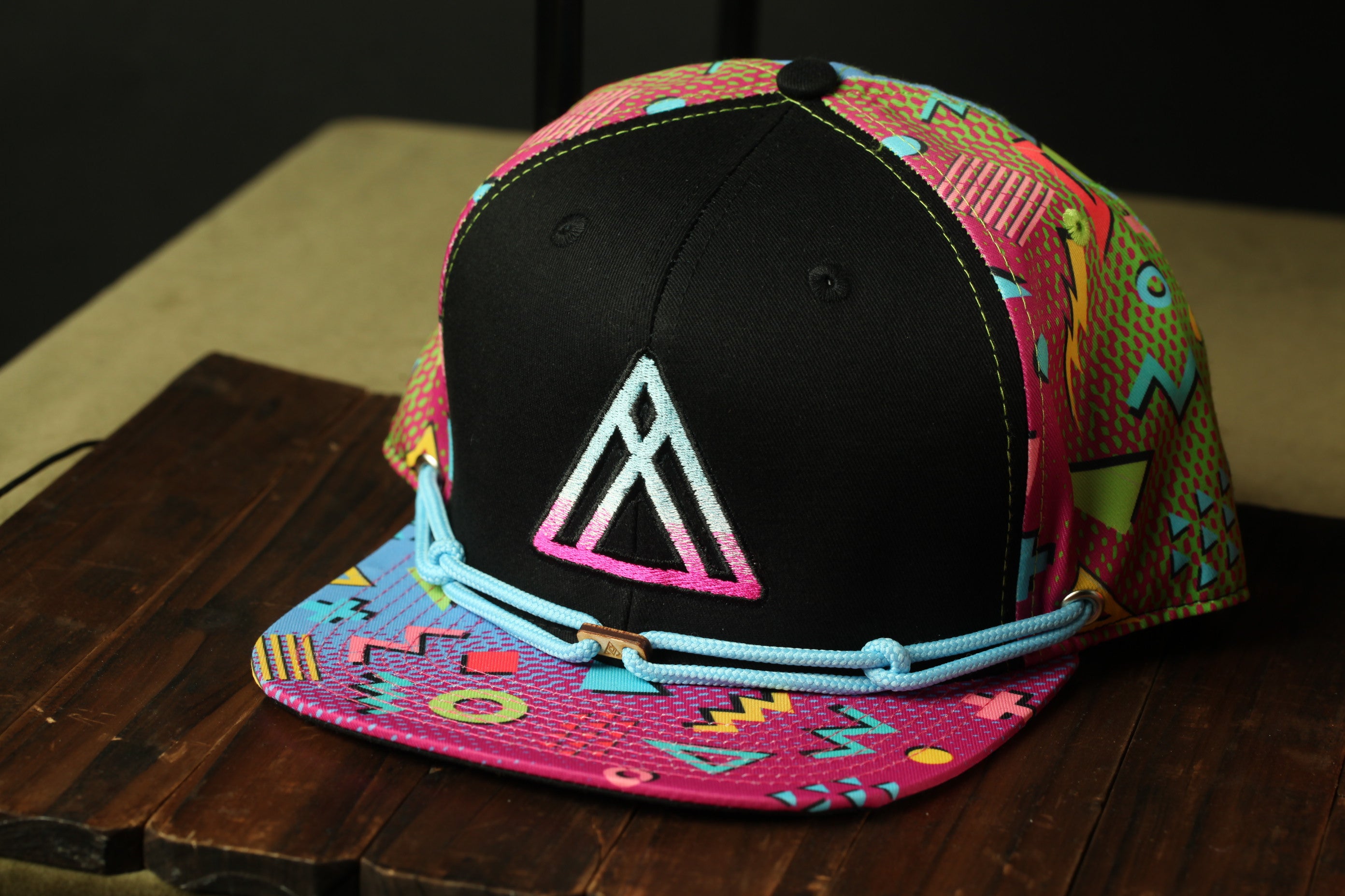 A colorful, patterned baseball cap with a black brim and a pink and blue geometric design on the front.