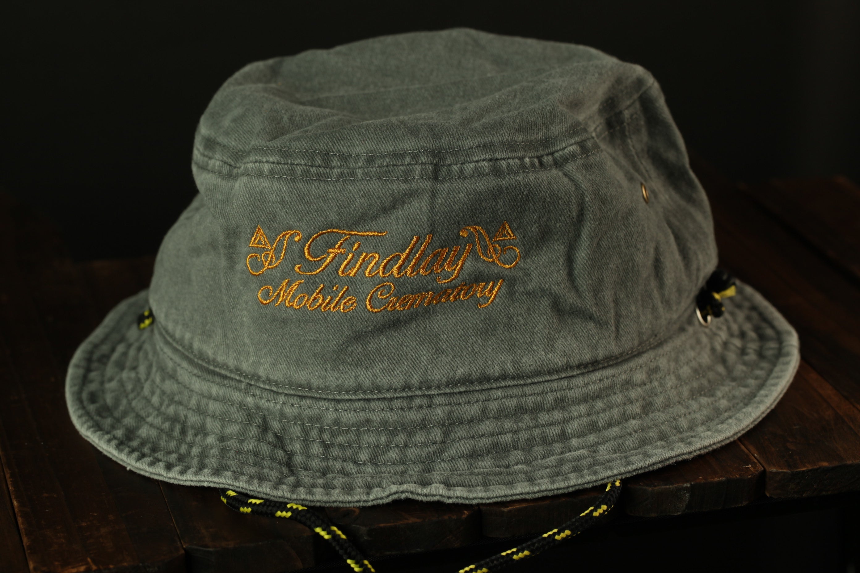 A gray bucket hat with the text "Findlay Mobile Company" embroidered on it, sitting on a wooden surface.