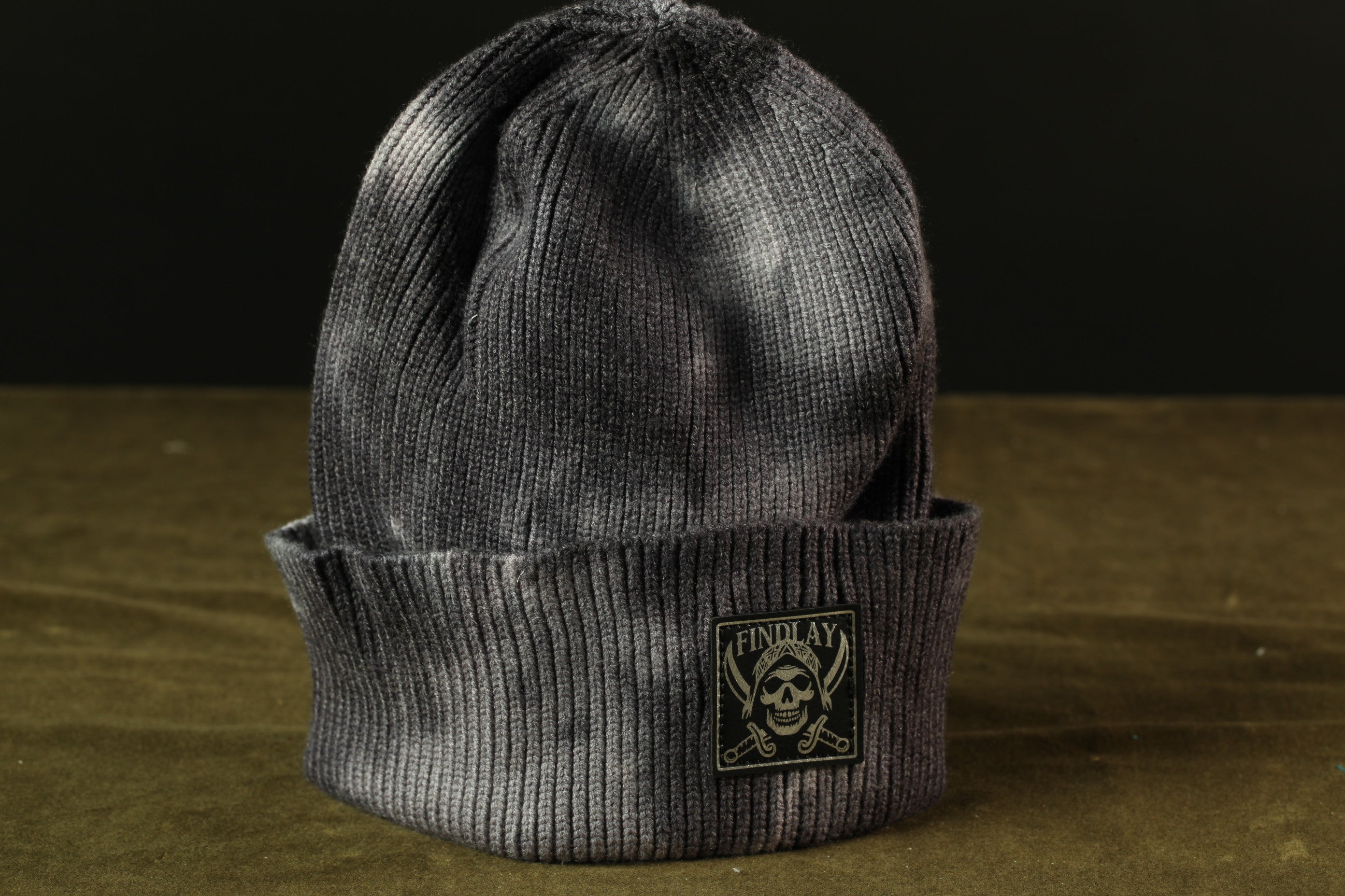 A gray knit beanie with a skull and crossbones design on the front, sitting on a brown surface.