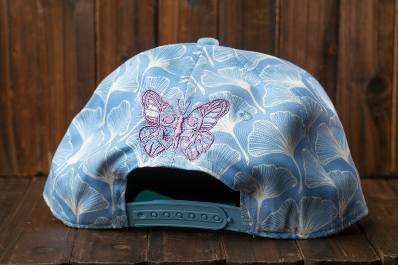 A blue baseball cap with a butterfly embroidered on it, placed on a wooden surface.