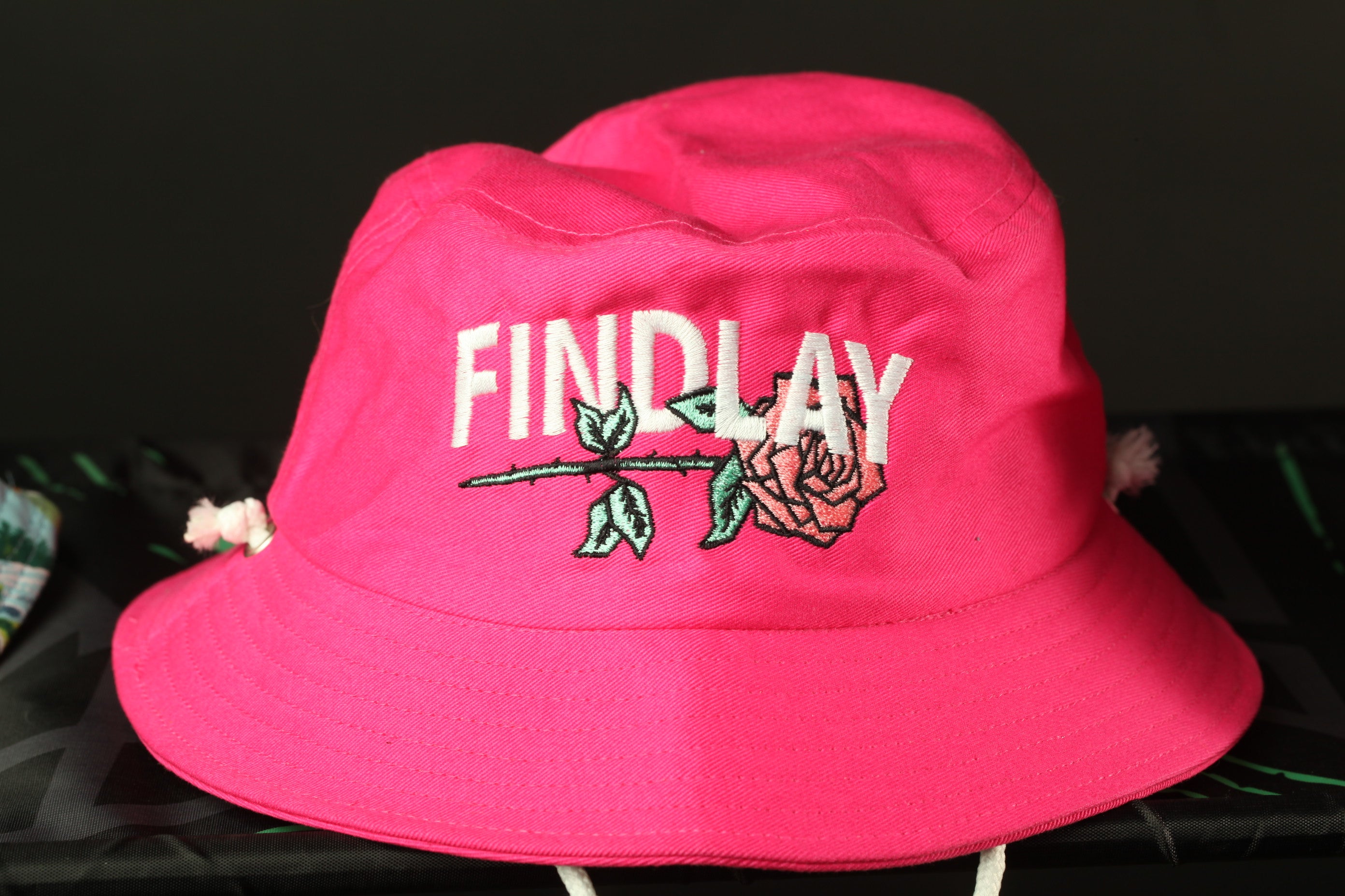 A bright pink bucket hat with the word "FINDlay" embroidered on it.