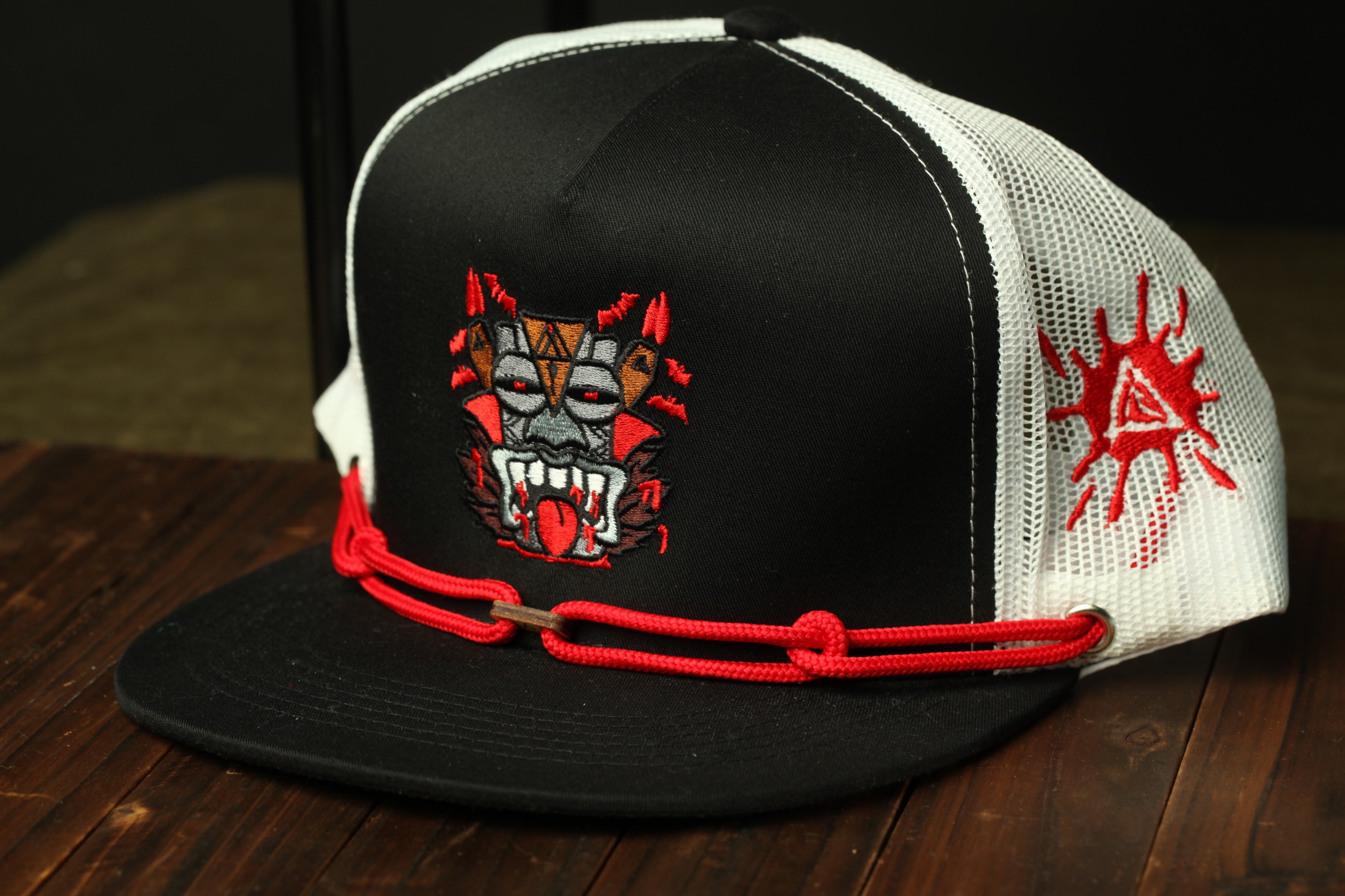 A black baseball cap with a red and white design on the front, featuring a stylized face with sharp teeth and an open mouth.
