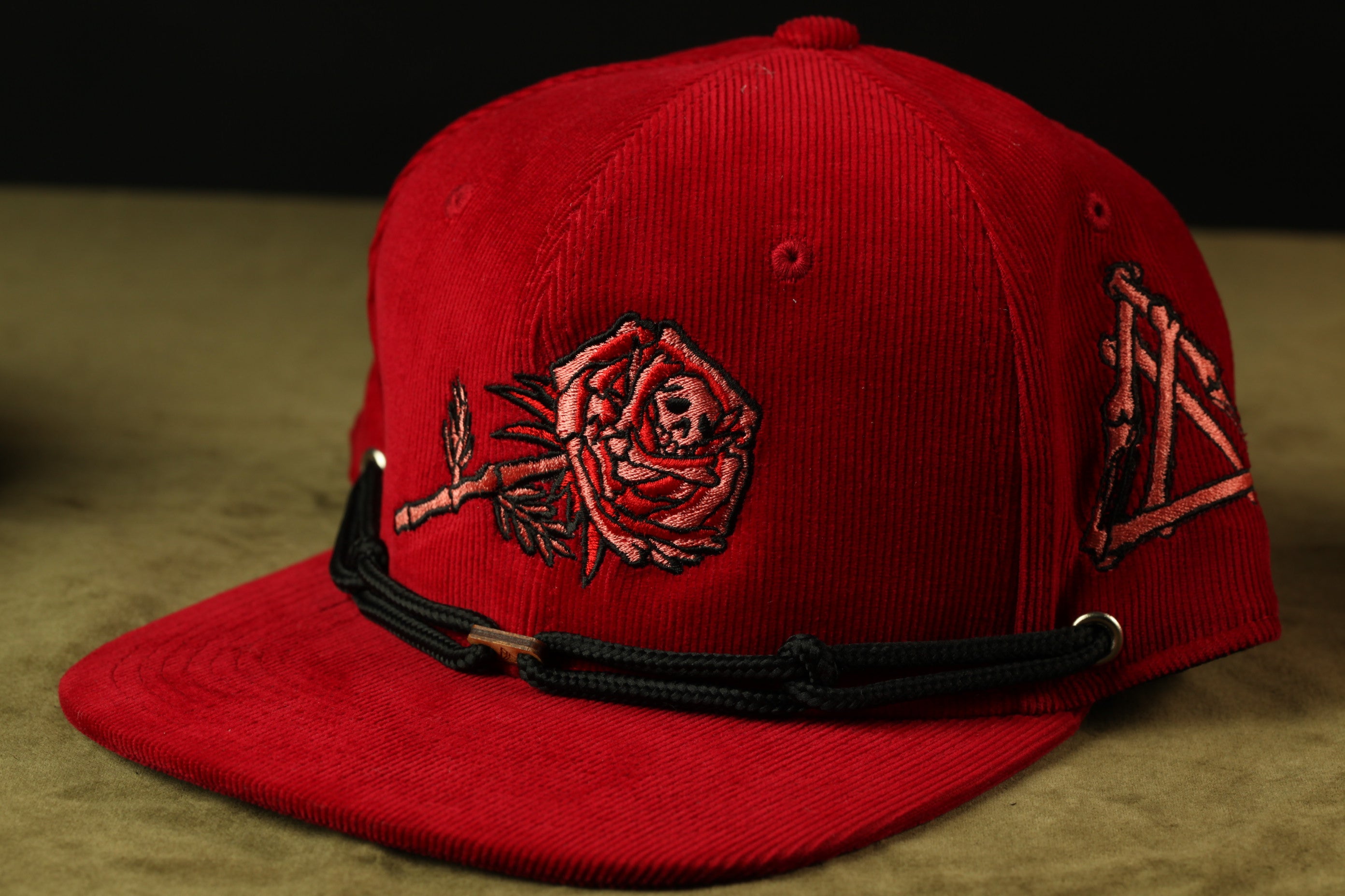 A red baseball cap with a rose embroidered on it, sitting on a surface.