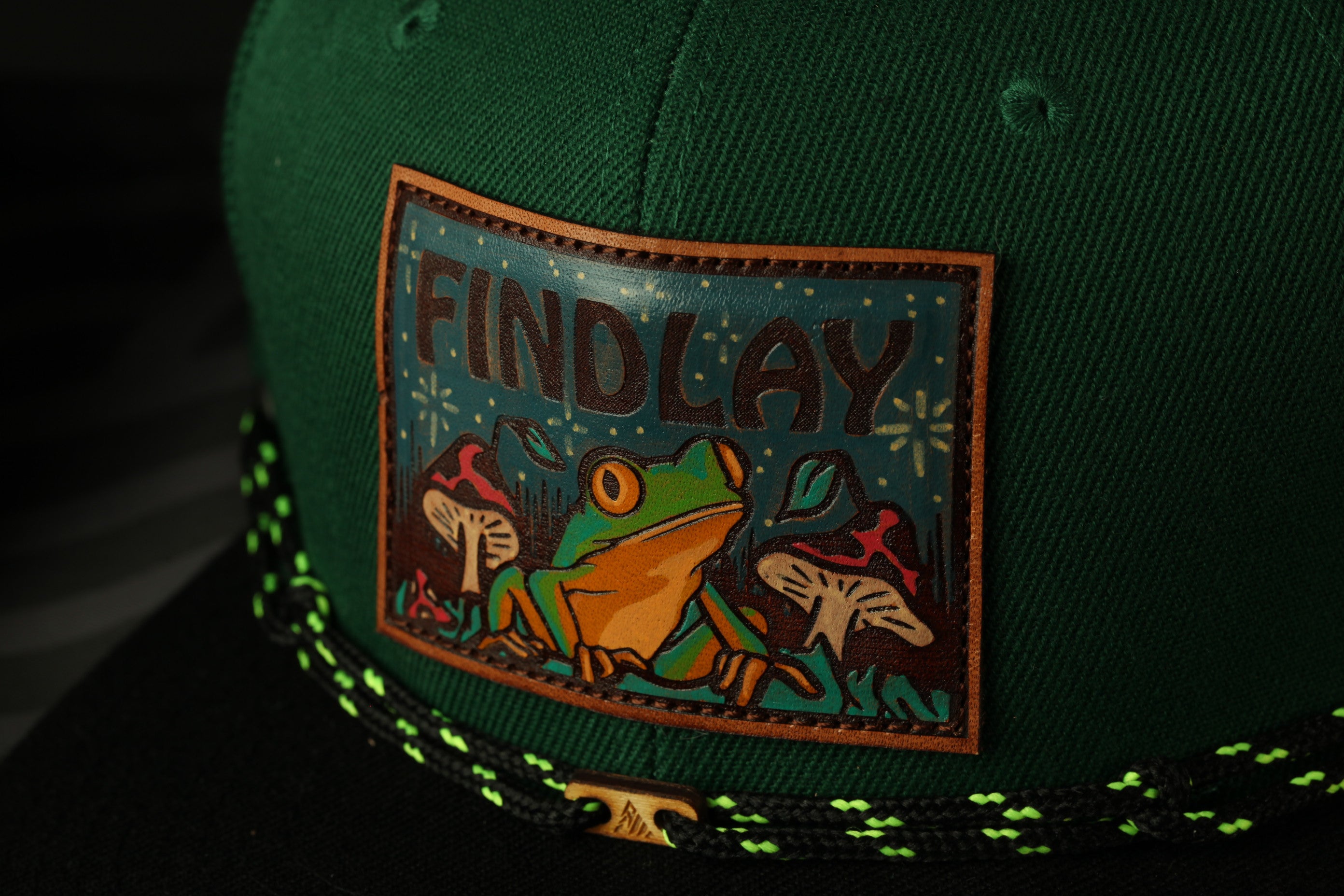A green baseball cap with a patch featuring a frog and mushrooms.