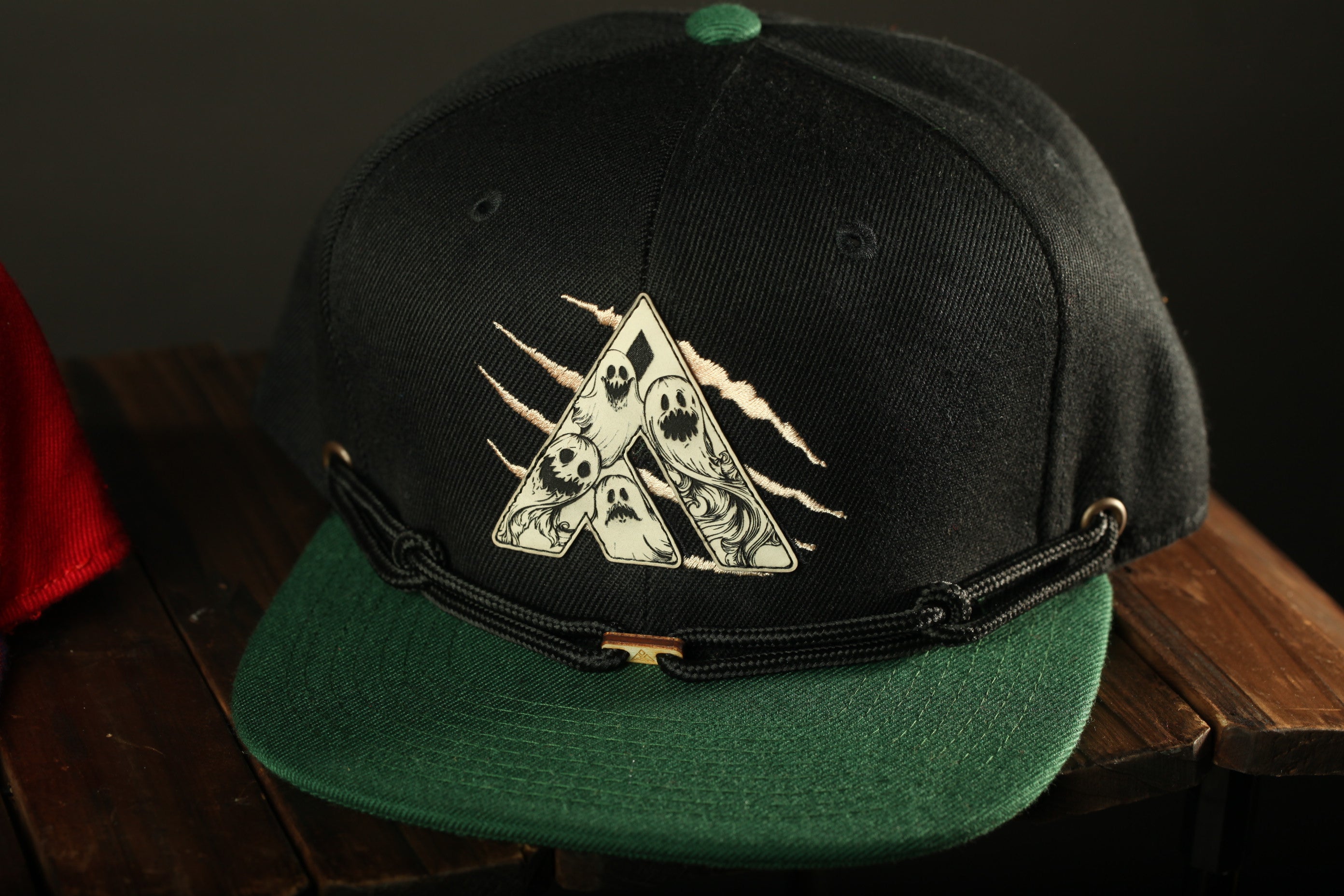 A black baseball cap with a green brim and a graphic design on the front, sitting on a wooden surface.