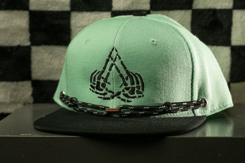 A green baseball cap with a black chain strap and a graphic design on the front.