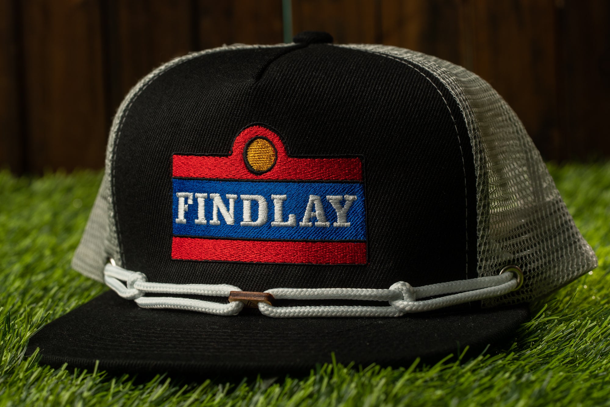 A black baseball cap with a red and blue patch that says "FINDLAY" on it, placed on a grassy surface.