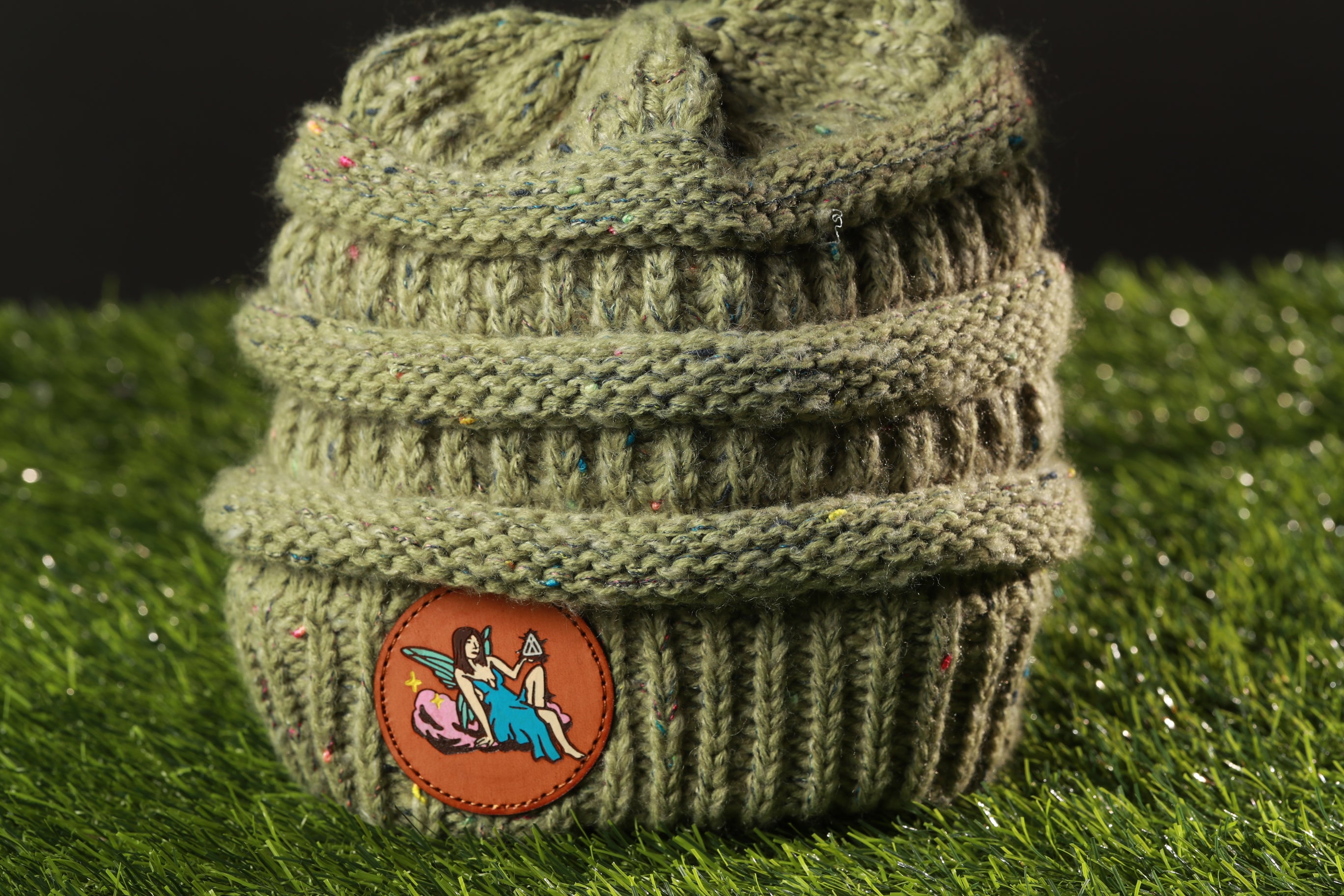 A knitted beanie with a circular patch featuring a cartoon character is placed on a green surface.